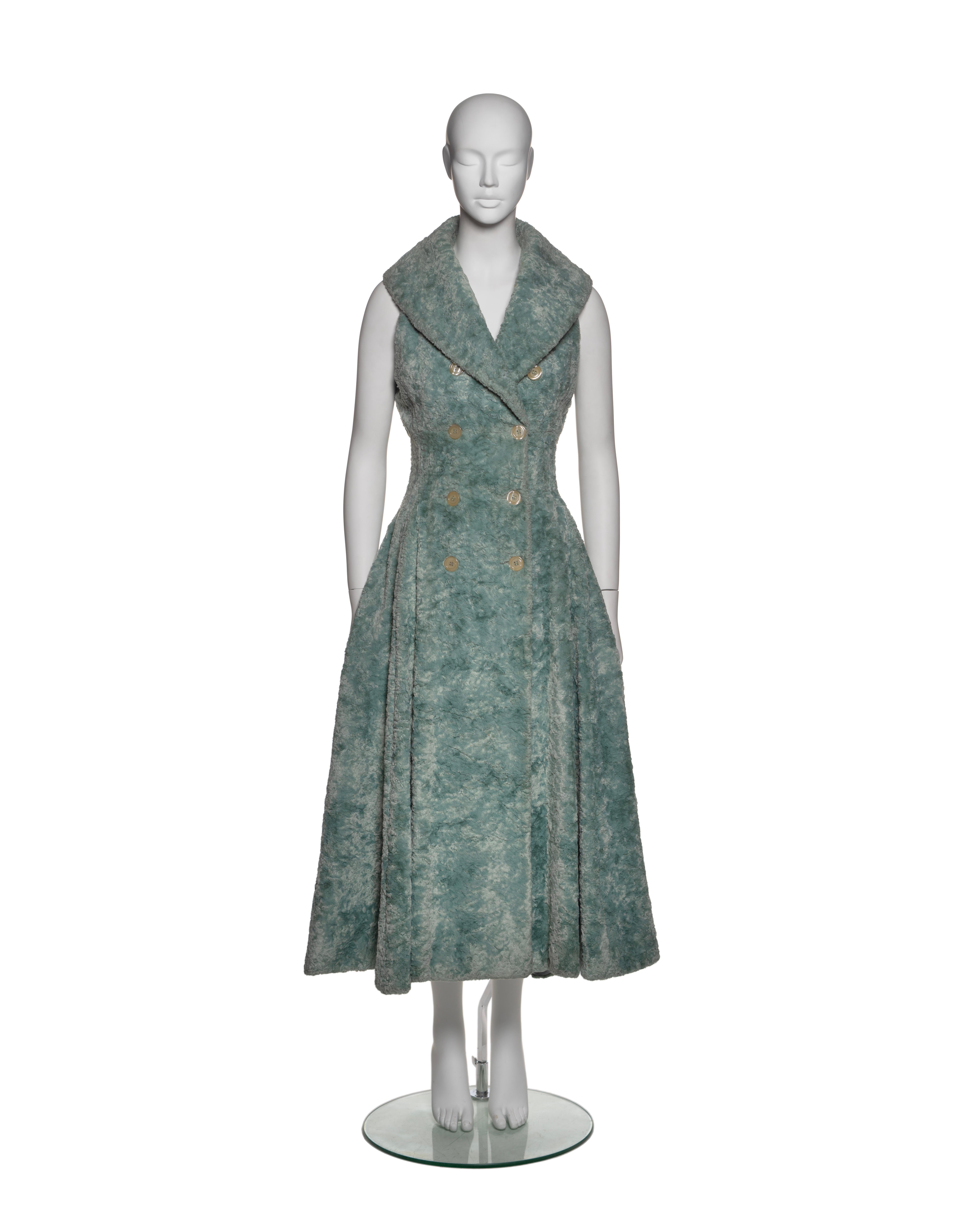 This Azzedine Alaïa coat dress from the Fall-Winter 1992 collection is made from a textured, plush fabric in muted seafoam green. It features a sleeveless, double-breasted design with a wide shawl lapel and neutral-toned buttons. The tailored bodice