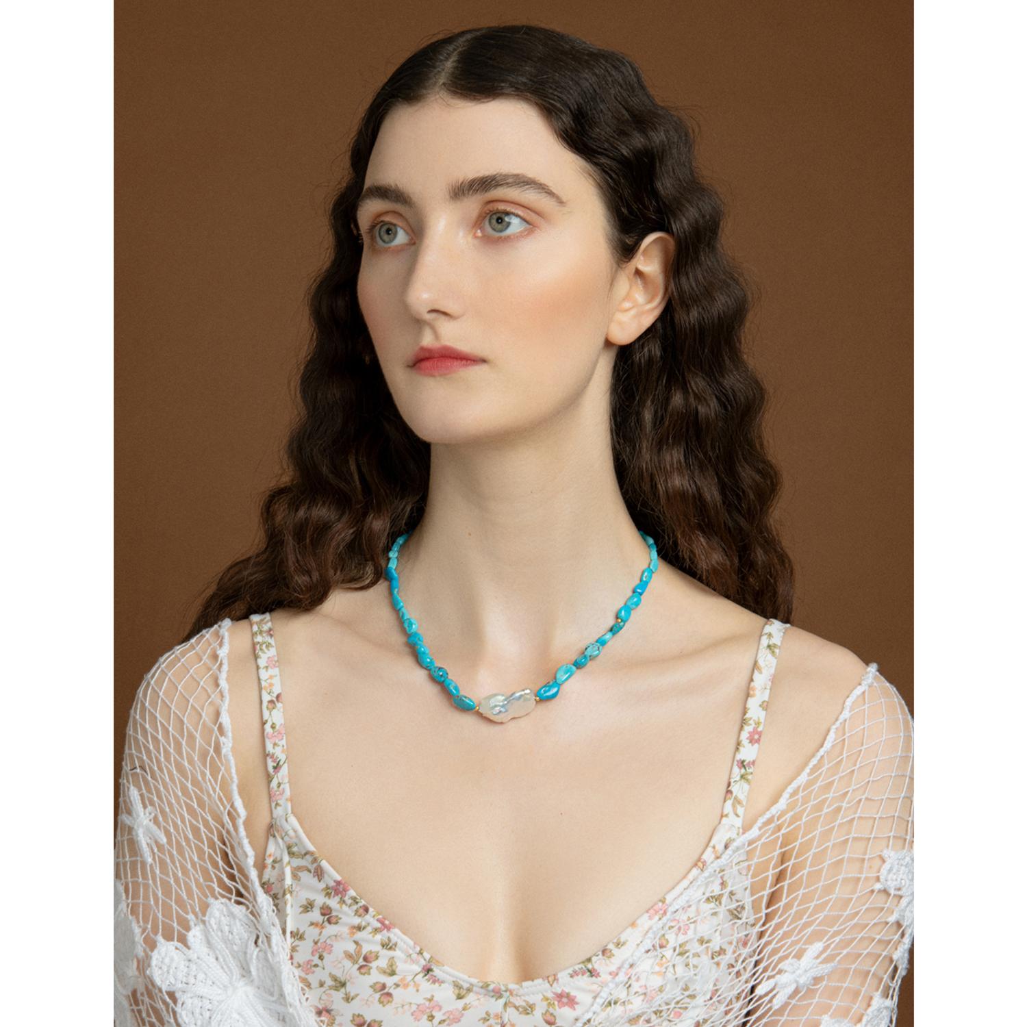 Indulge yourself in timeless elegance with this Azzurra necklace by Vintouch Jewels. Handmade from 18-karat gold, this necklace is strung with turquoise beads, each unique in its own way. At the center is a glossy baroque pearl, which symbolizes