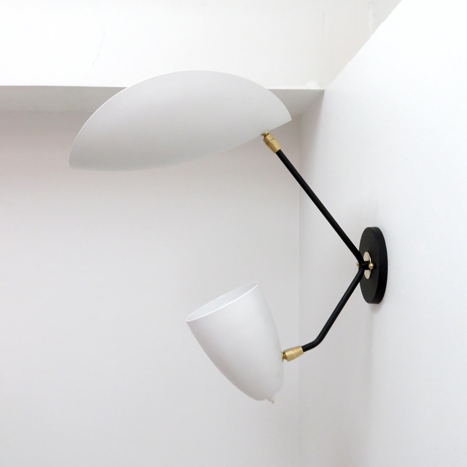 Wonderful asymmetrical double arm wall lights by Gallery L7, handcrafted and finished in Los Angeles from American brass with one fully adjustable two-tone cone shade and one reflector shell light, both in egg shell with white powder coated