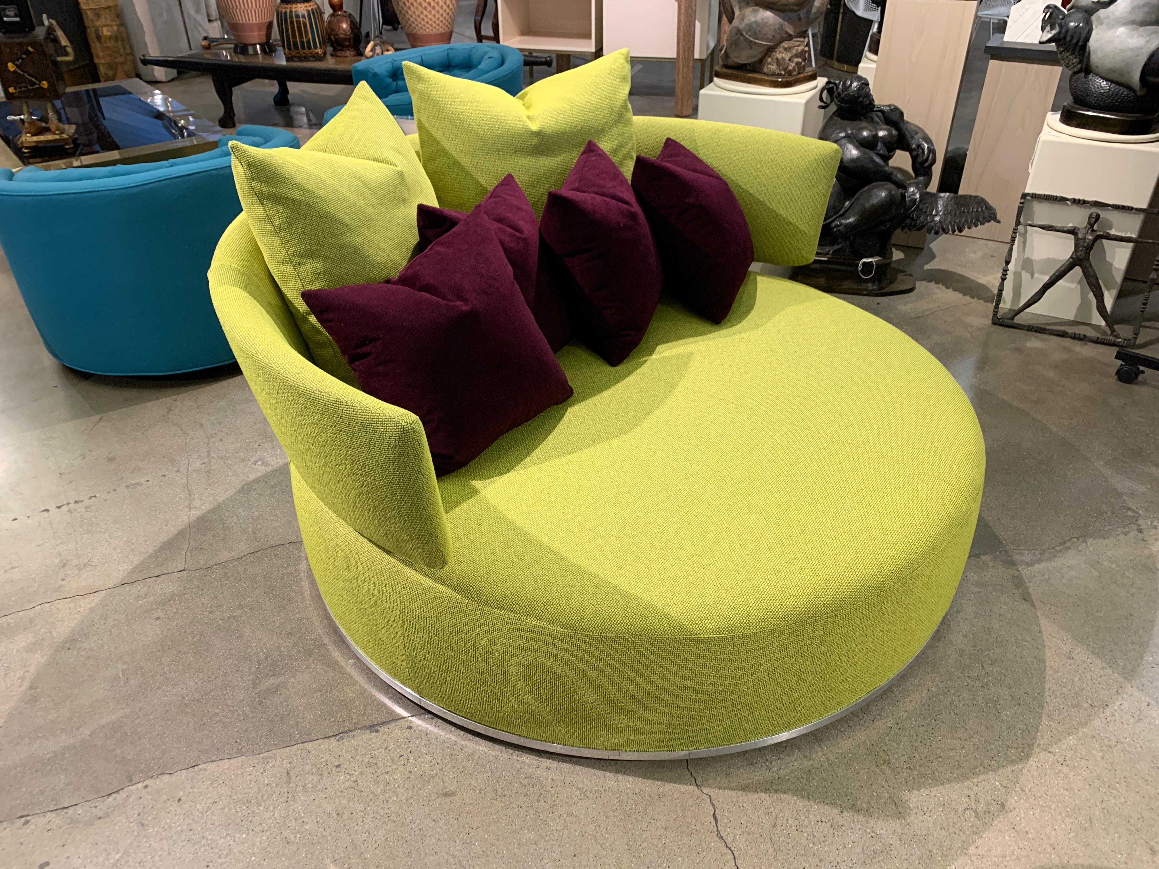 A beautifully re-upholstered B & B Italia round sofa designed by Antonio Citterio for their Maxalto line called the Amoenus. It has been redone in a citrus color fabric with purple accent pillows. The sofa swivels and rolls as it os on castors as