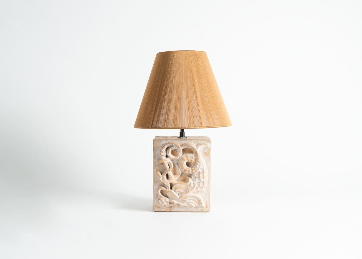 Cette lampe en grès présente des éléments nautiques en relief, notamment un poisson stylisé, une ancre de bateau et un gréement. Signé : B. Chalvet