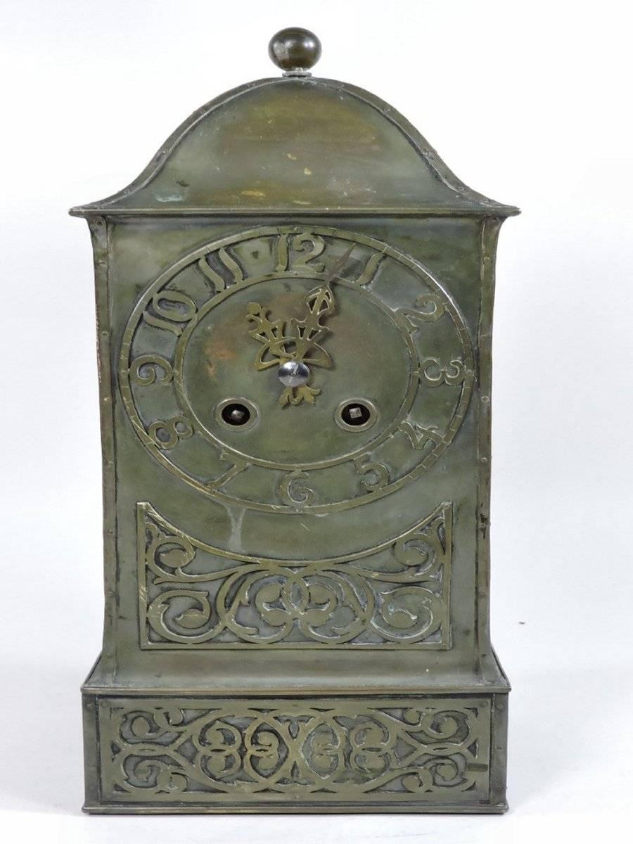 Birmingham guild of handicraft, attributed. 
An Arts and Crafts hand made brass mantel clock, with ball finial, stylised floral hand chased decoration and hand riveted construction throughout with stylised hinges to the door and initials to the