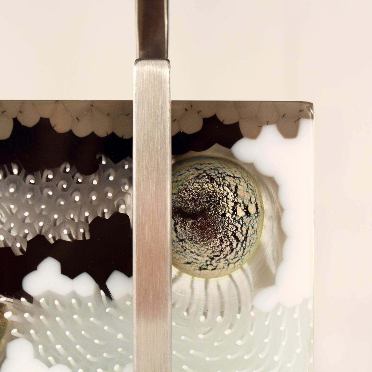 Lampe de table B-lock. 60 cm de long, bloc en verre de Murano artistique, abat-jour en organza gris foncé et base en hêtre blanc.
Le bloc de verre artistique de Murano est une expression créative et naturelle de la murrine et des tiges de verre