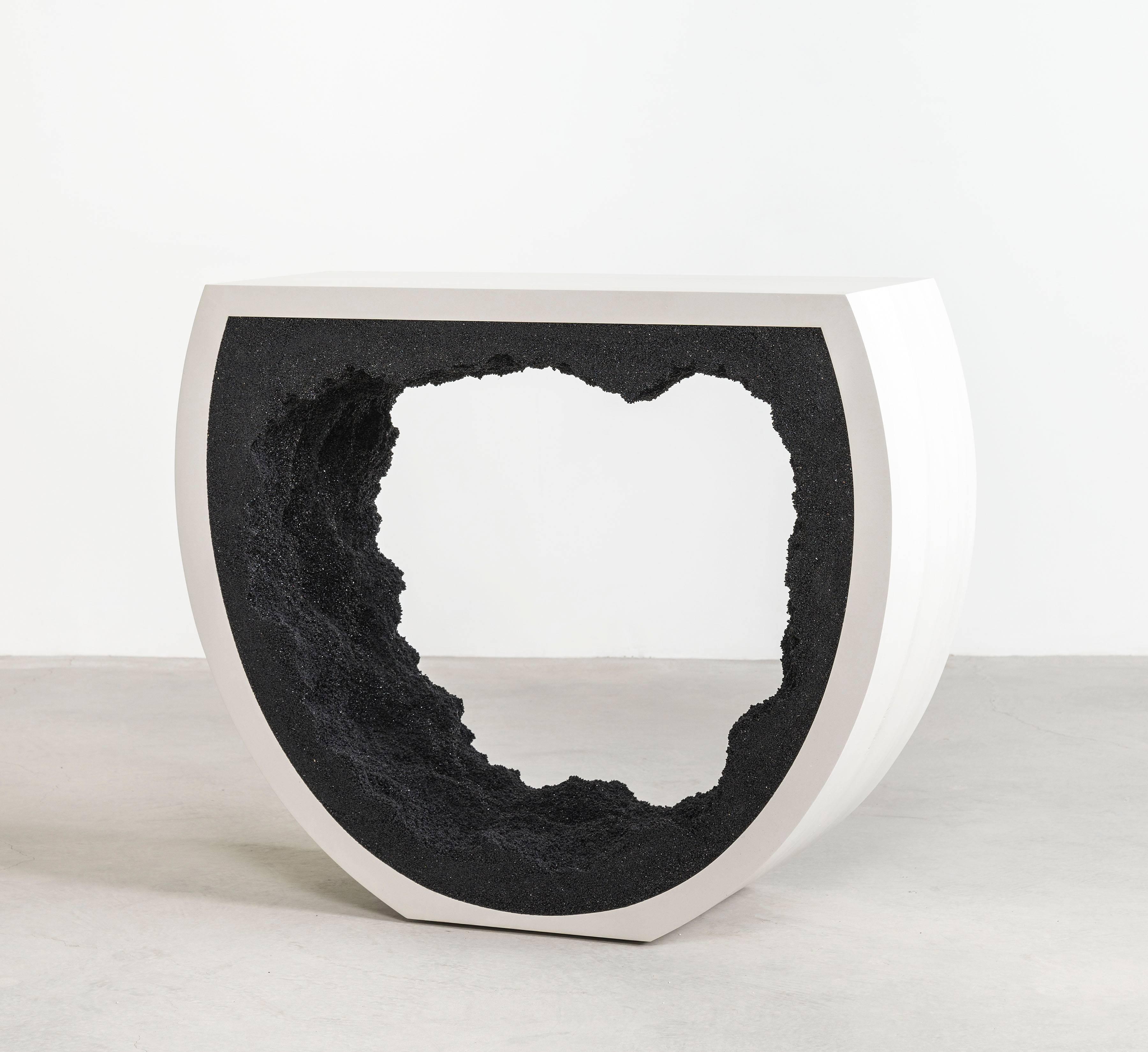 Composta da una combinazione di materiali, la console a semicerchio è composta da un esterno in cemento tinto a mano e da un interno in silice. Impacchettata a mano all'interno del cemento bianco e liscio, la silice nera forma una texture organica