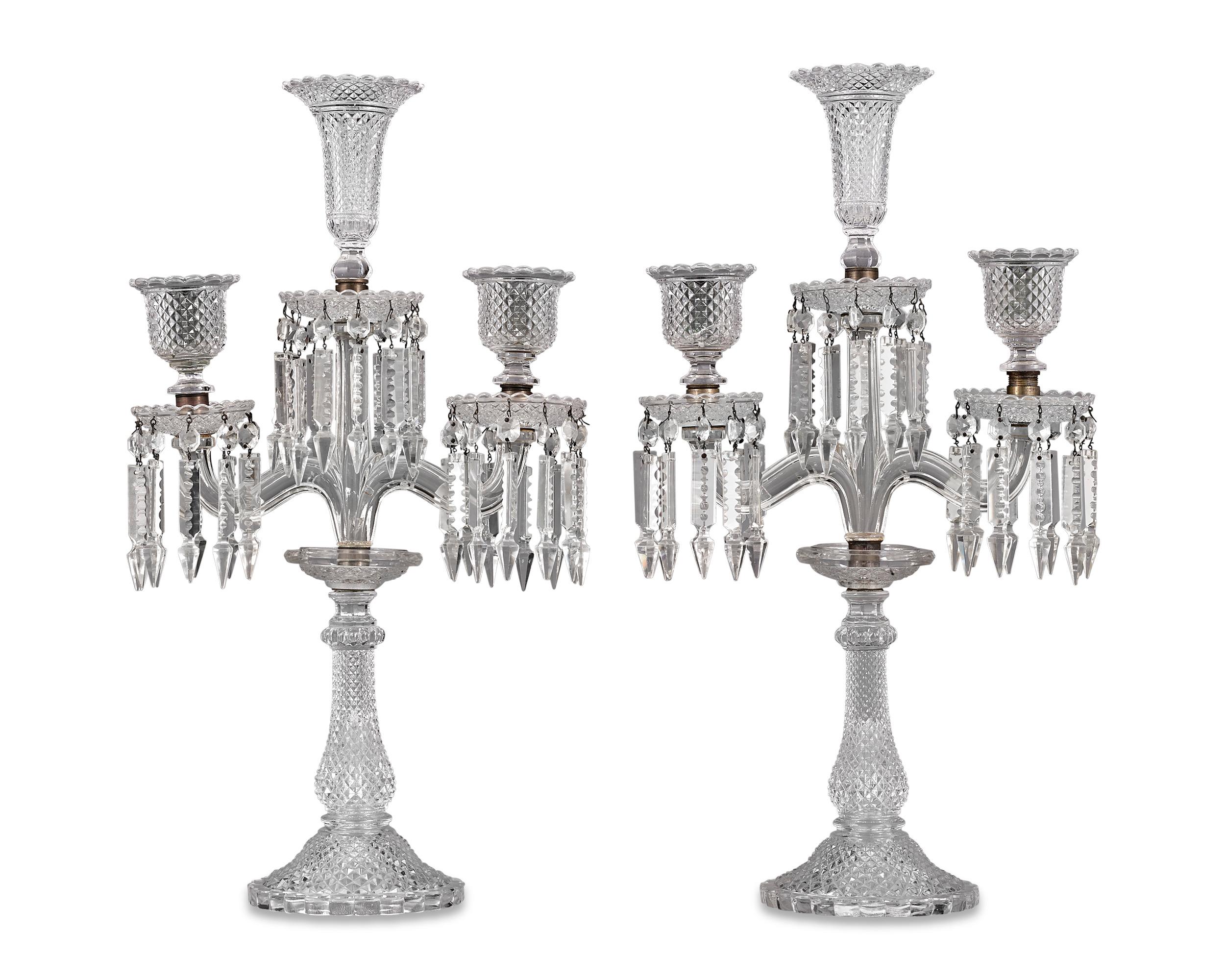 This pair of baccarat three-light candelabra is crafted from some of the most dazzling crystal ever made. Brilliantly faceted crystals hang from each of the three bases, which hold aloft exquisitely cut tulip-shaped candleholders. The calibre and