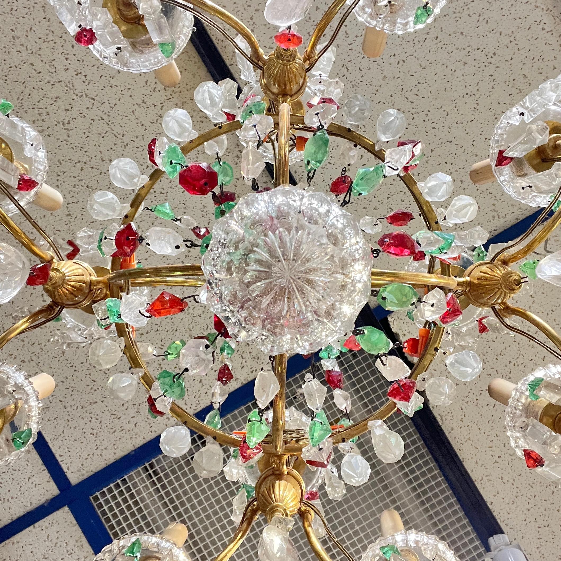 Antigüedades francesas de gran calidad  araña de Baccarat en bronce dorado con ocho casquillos electrificados que alojan bombillas de tamaño candelabro, y que se distingue por sus gotas y guirnaldas facetadas de cristal rojo, verde y transparente. 