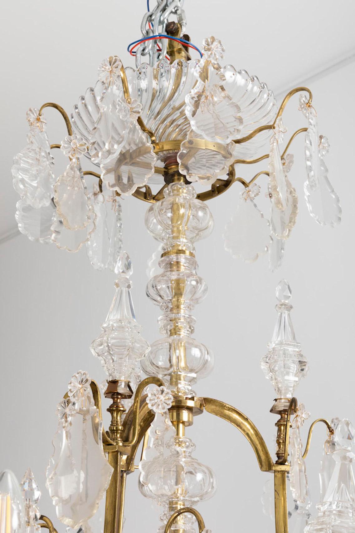 Baccarat, signed.

Large Louis XV style cage chandelier with 18 fires on two levels with a curved shaped gilt brass structure.
Crystal cache-bélière (hide-hook) in a shape of a large twisted gadroons cup supported by a gilt brass circular ring on