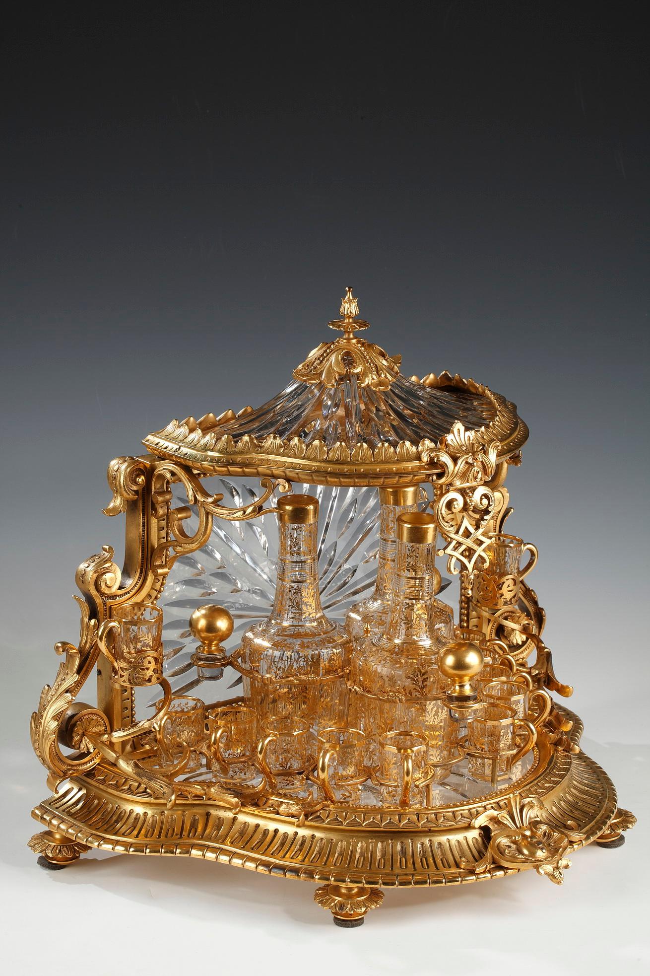 Rare dome-shaped liquor casket entirely in cut crystal, enriched with a beautiful gilded bronze mount with scalloped lines decorated with friezes of water leaves, beads, scrolls and shell. It includes three carafes and twelve faceted cut crystal