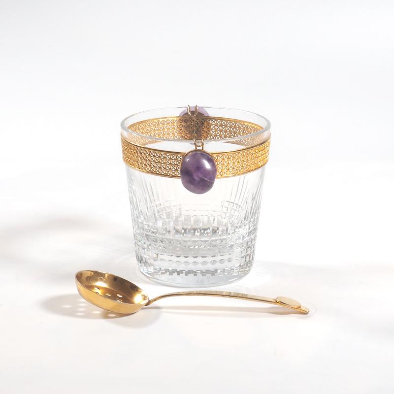 A distinctive and highly unusual Baccarat crystal and gilt mounted ice bucket with amethyst handles and accompanying gold plated slotted ladle. The renowned Baccarat 'Nancy' design of deep cut crystal is enhanced by the Fine filigree geometric gold