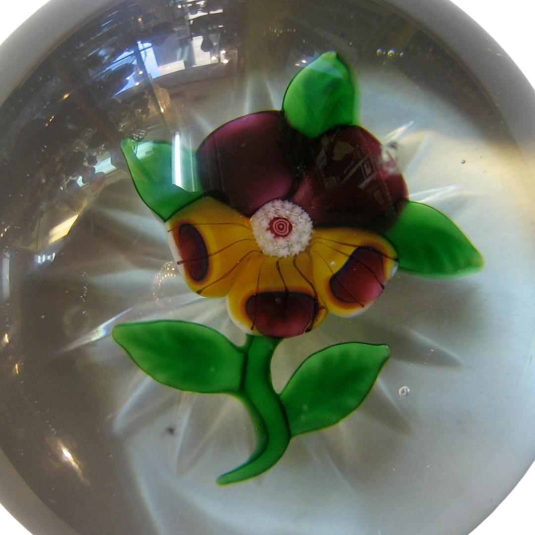 A single pansy Baccarat paperweight
Two large dark purple upper petals and three purple-tipped yellow lower petals,
each accented with three thin black lines with a white stardust and bull's-eye cane centre.
Three small, spaced green leaves