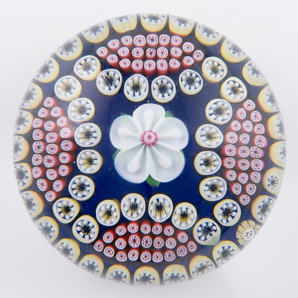 Titolo : Baccarat fermacarte Fiore Millefiori Quarti 1980
Data: 1980
Origine: Francia
Caratteristiche : Un fiore centrale bianco lavorato a lume di candela  circondato da  quattro archi acquartierati di canne millefiori policrome, con un anello