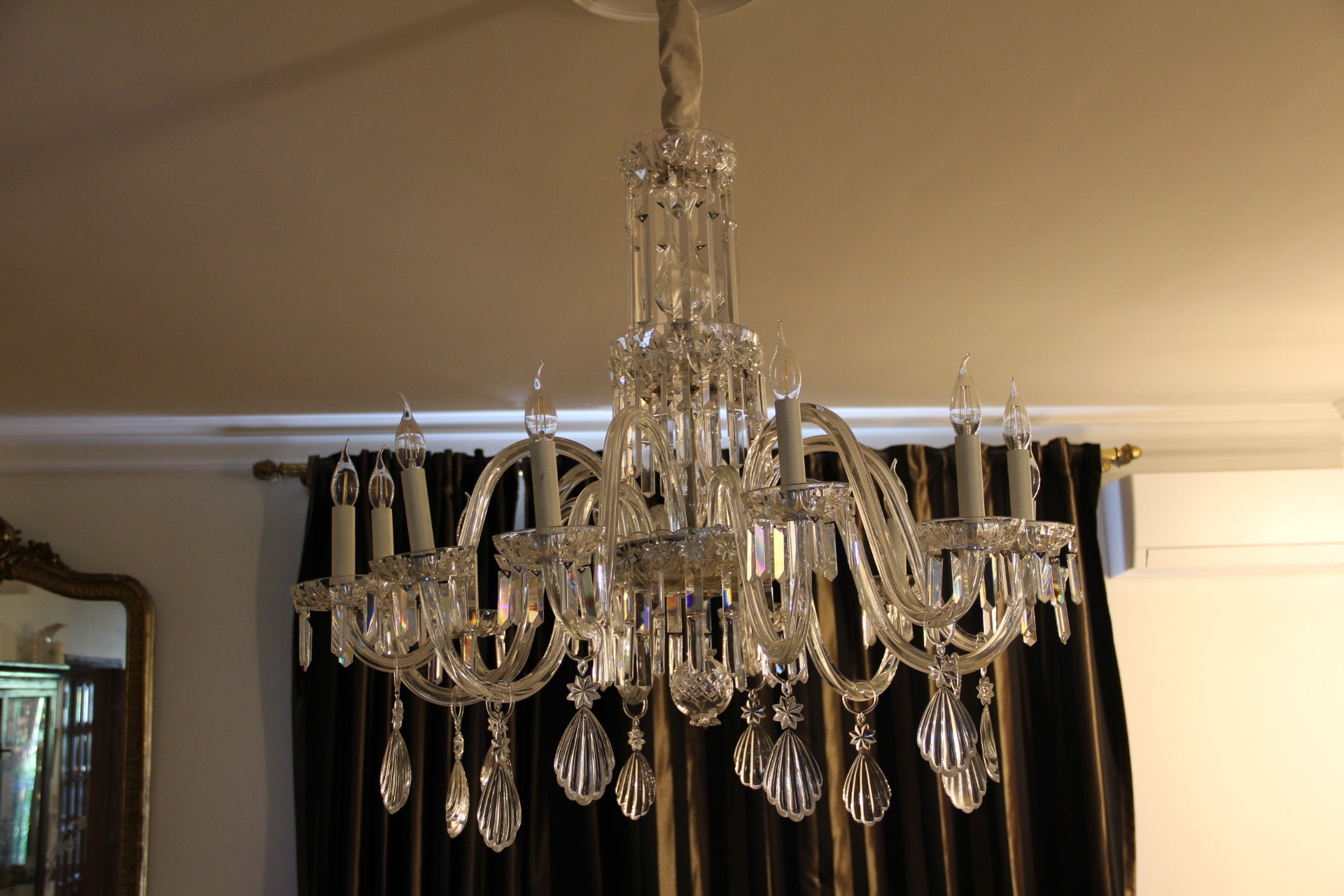 Questo lampadario di cristallo mozzafiato a dodici luci è caratterizzato da bracci in vetro curvato che si espandono elegantemente da un elemento centrale impilato interamente in cristallo con tre corone circostanti di pendenti in cristallo a forma