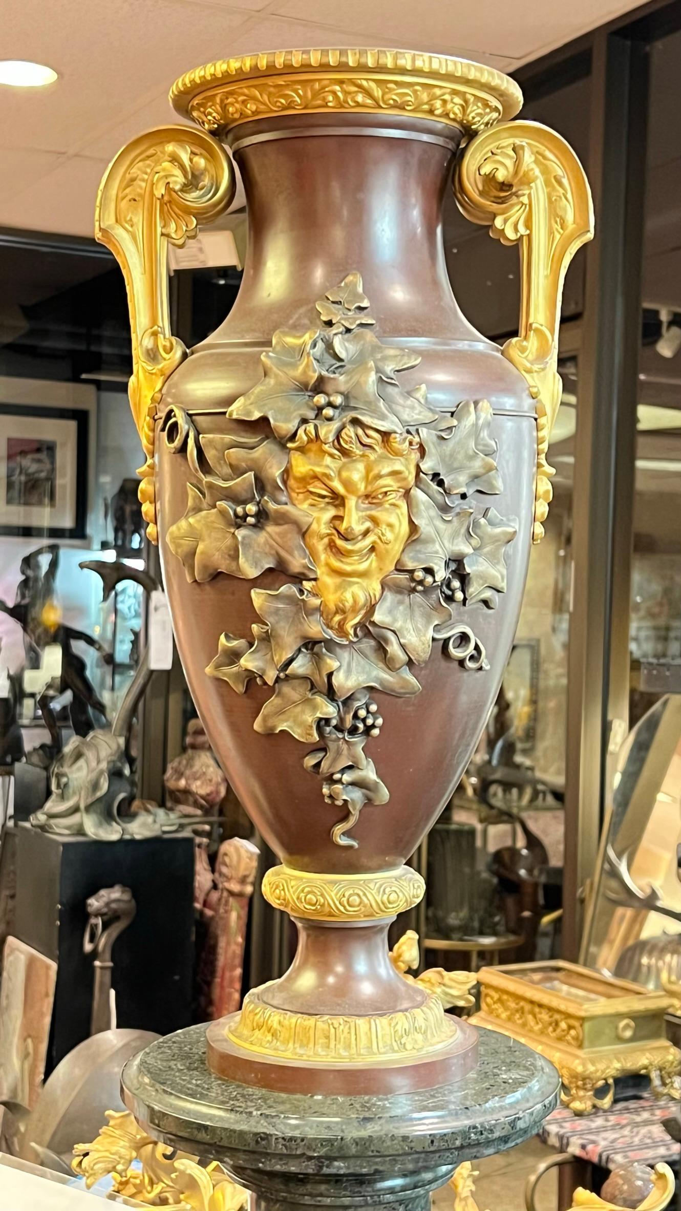 Unsere Mittelstück-Vase, die Ferdinand Barbedienne um 1870 zugeschrieben wird, zeigt eine ausdrucksstarke Bacchus-Maske, die von versilberten Weinreben umgeben ist, prominente vergoldete Bronzegriffe mit Akanthusblatt- und Glockenblumenmotiven sowie