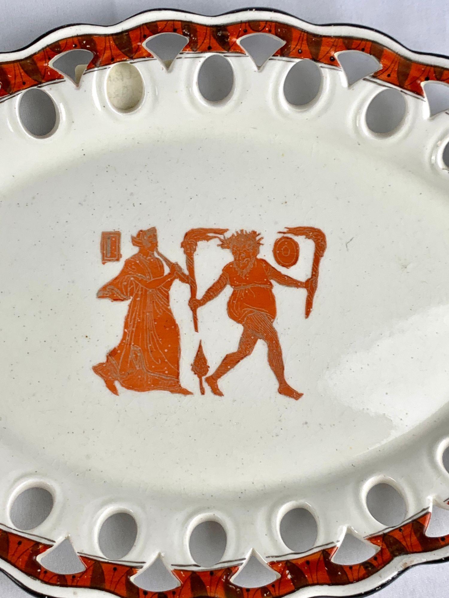 Cette ancienne assiette anglaise en faïence, vers 1820, présente une scène de Bacchanale d'un rouge vif, encadrée d'une élégante bordure réticulée à motif géométrique ajouré.
Au centre, une maenade drapée joue de la flûte, symbolisant son rôle
