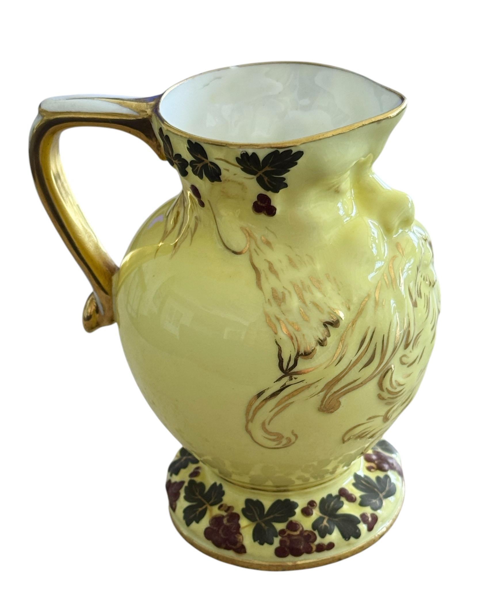 This unique porcelain pitcher in rich yellow is beautifully accented with purple grapes and green leaves along the foot and rim, complemented by delicate gold gilt trim. A truly remarkable find. The front features an embossed bearded face, believed