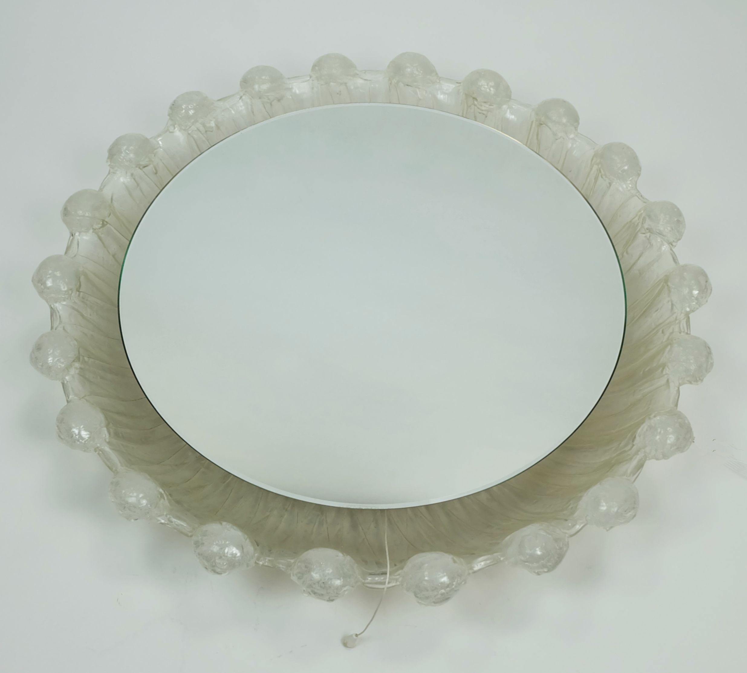 Very nice decorative wall mirror from the 1960s/70s. With manufacturer's label Schöninger. Round shape. Acrylic frame with an ice glass look. The mirror is backlit with 4 E14 bulbs (not included). It can be switched on and off using a drawbar
