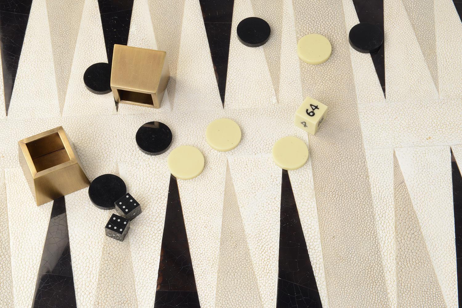 Le plateau de jeu de backgammon KIFU PARIS est le jeu de luxe par excellence. Agrémentée d'un mélange de galuchat, de coquille de stylo et de laiton bronze-patine, cette pièce est livrée avec toutes les pièces du jeu dans une pochette en velours.