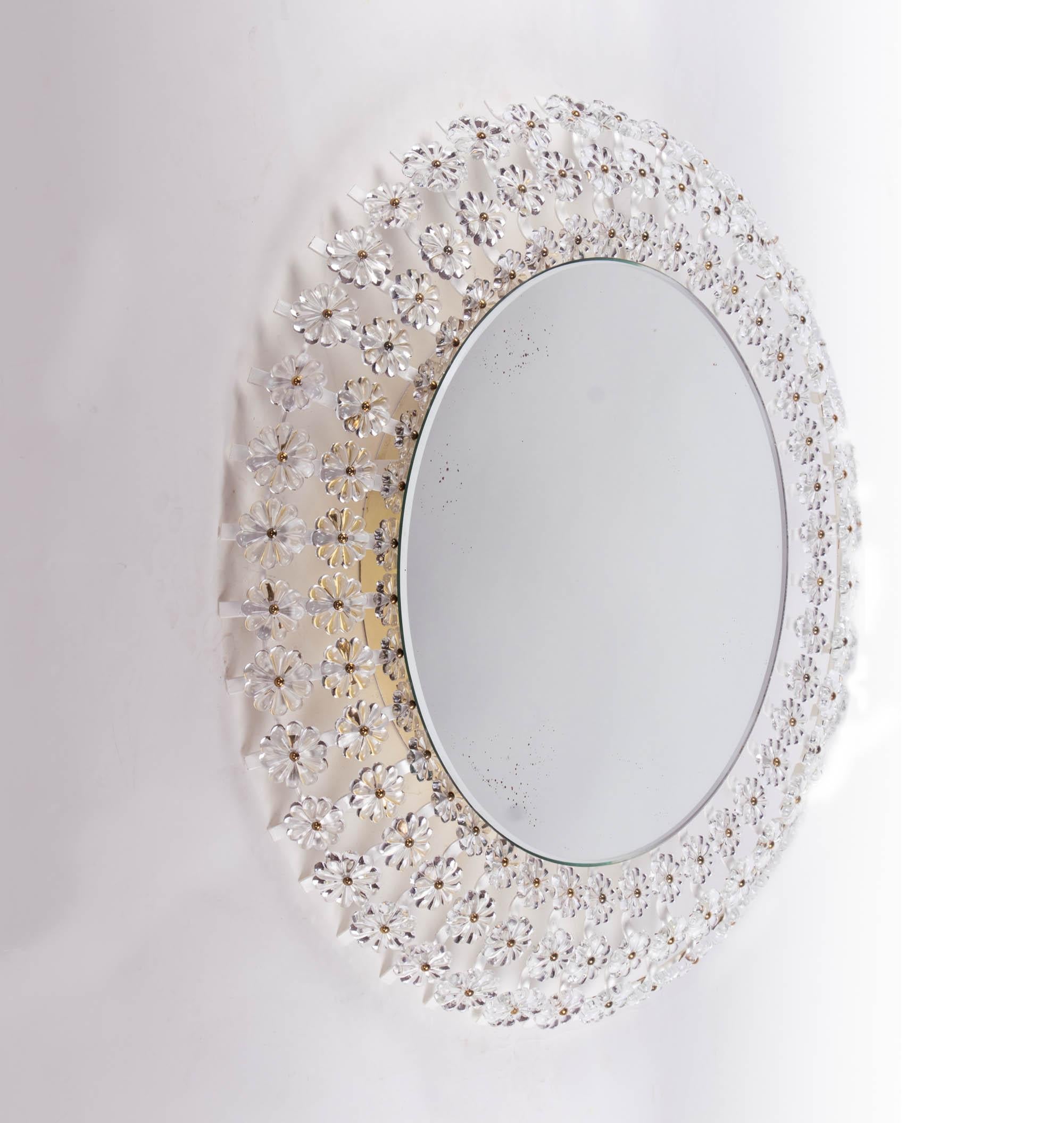 Gorgeous illuminated mirror in mid-century style surrounded by countless crystal flowers on a round mirror with an enameled metal frame. The backlit glass flowers arranged all around are reminiscent of a sunburst pattern. Rare design. The Mirror