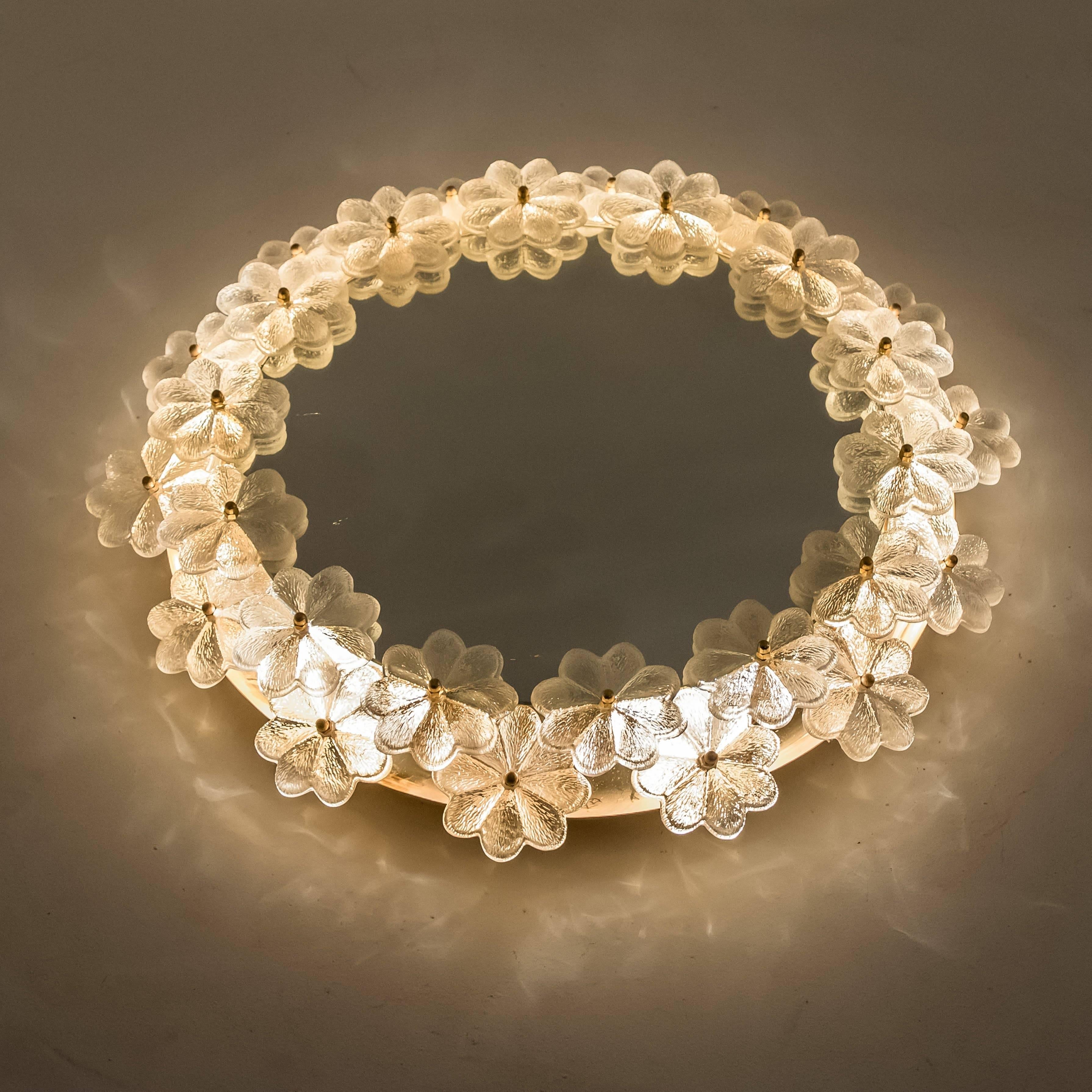 Illuminated or backlit mirror by Ernst Palme, Germany, 1970s.

The mirror sits in the center of a brass frame surrounded by 28 glass flowers of approximately nine cm diameter, each screwed into the frame with a decorative pin making the center of