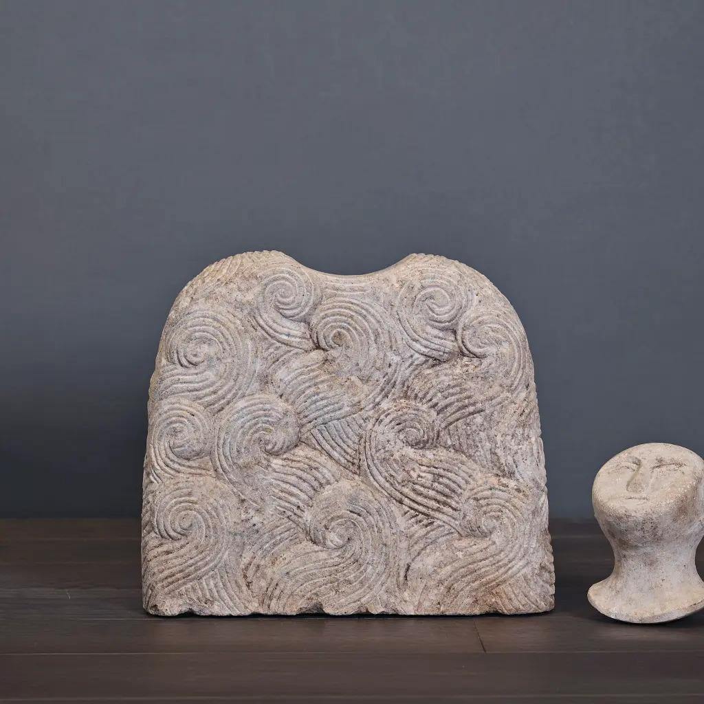 This sandstone Bactrian idol is a handcrafted reproduction inspired by ancient votive statues from the region of Bactria, in present-day Afghanistan. Carefully carved and finished with an aged patina, it features a trapezoidal body engraved with