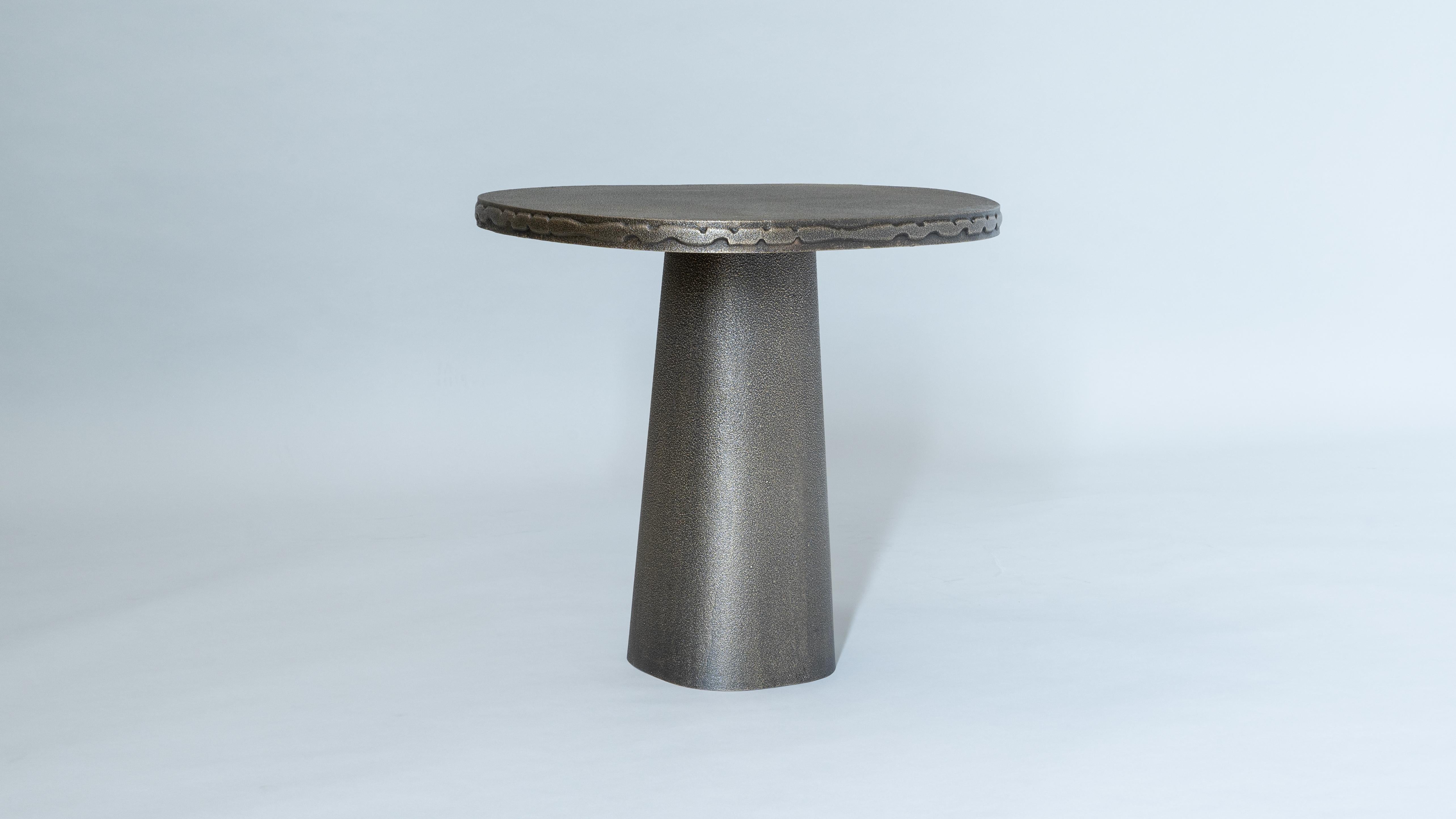 Cast entirely in bronze, the Badal Side Table is a study in the textural possibilities of metals, realized with intricate surface patterns and a raised band of decorative patterning on it’s edge.