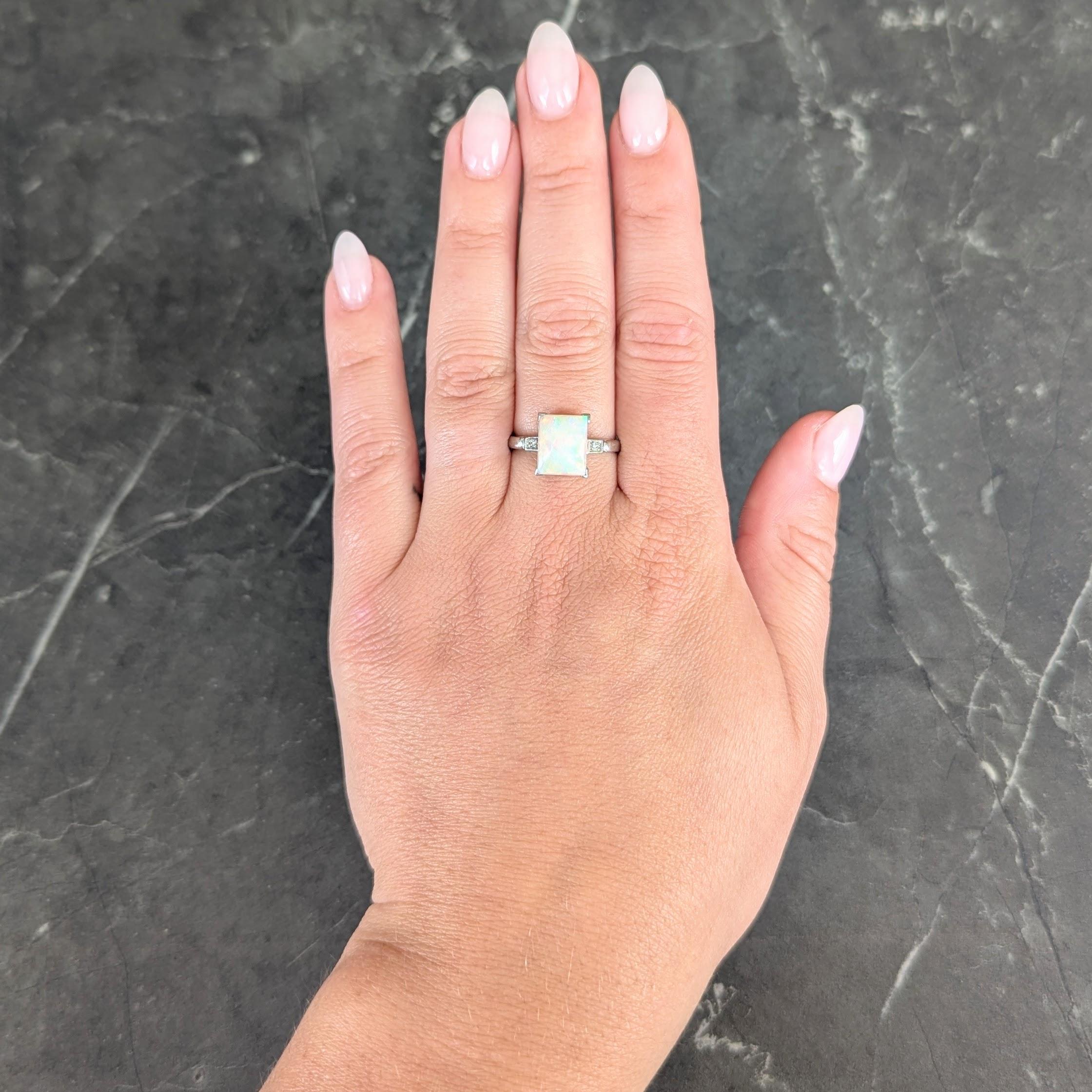 Centering a rectangular shaped opal cabochon measuring 10.0 x 8.0 mm
Translucent white in body color with spectral play-of-color
Prong set in basket and flanked by cathedral shoulders
Bead set with single cut diamonds in square forms
Weighing