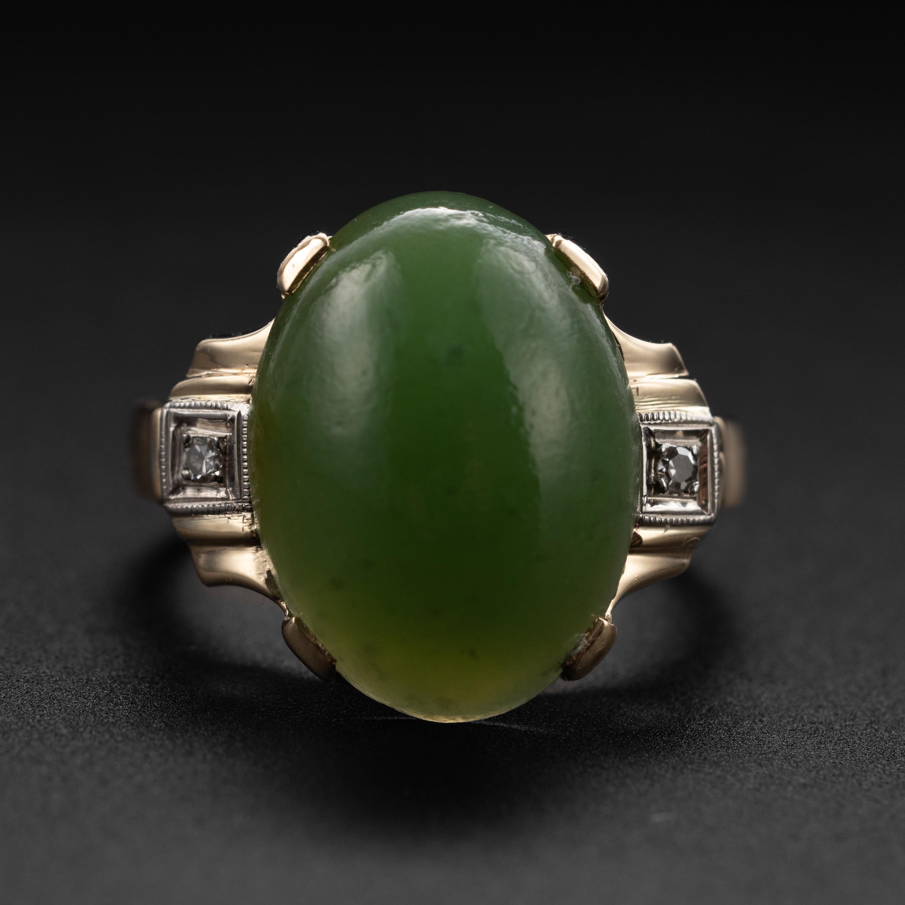 This late Deco / early Retro ring (circa 1940) was created by New York jewelry firm, Baden & Foss. Featuring a 16.24mm x 11.98 cabochon of a medium green tone, prong-set and flanked on both sides with a pair of tiny old single-cut diamonds, this 14K