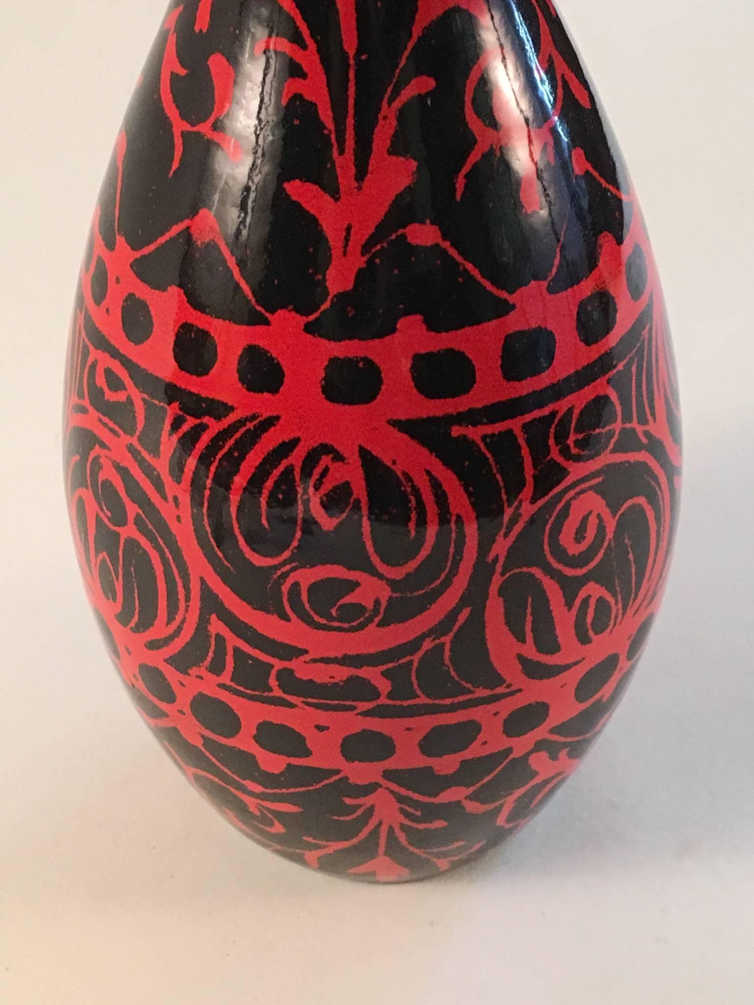 A bottle shaped vase with a ring neck, reminiscent of an 18th century glass decanter, in black with a red swirl pattern glaze. With its original Raymor label.
