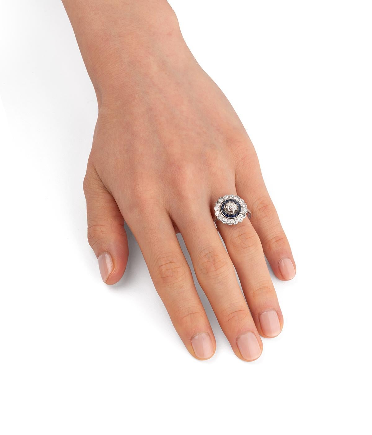 Bague de fiançailles ancienne en platine du début du 20ème siècle. De forma festoneada, está centrada en un diamante de cola antigua de aprox. 0,5 quilates (estimado I - VS) rodeado de una línea de zafiros calibrados y de una línea de diamantes de