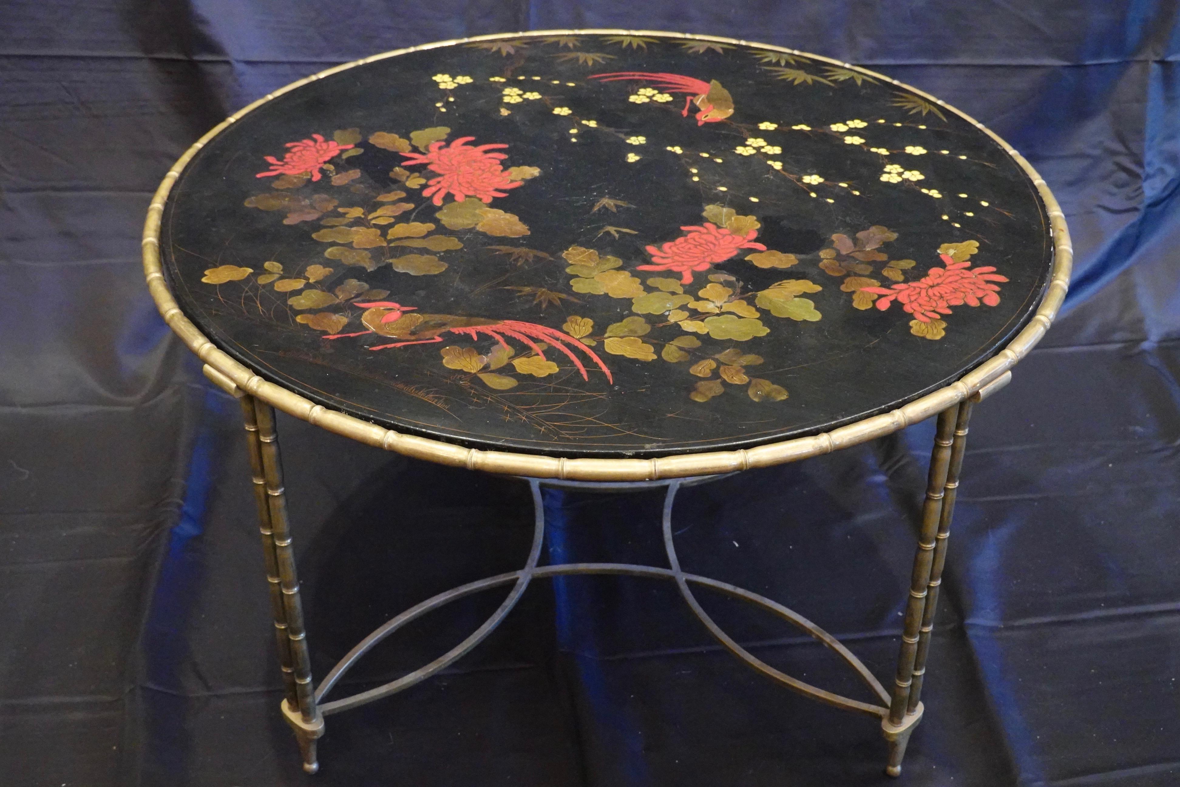 Lovely French round cocktail or coffee table with colorful Japanned lacquered top surface in black ground, featuring red birds and peonies, yellow flowers and bamboo leaves. The frame of the table is nicely-cast faux bamboo in bronze, supported by