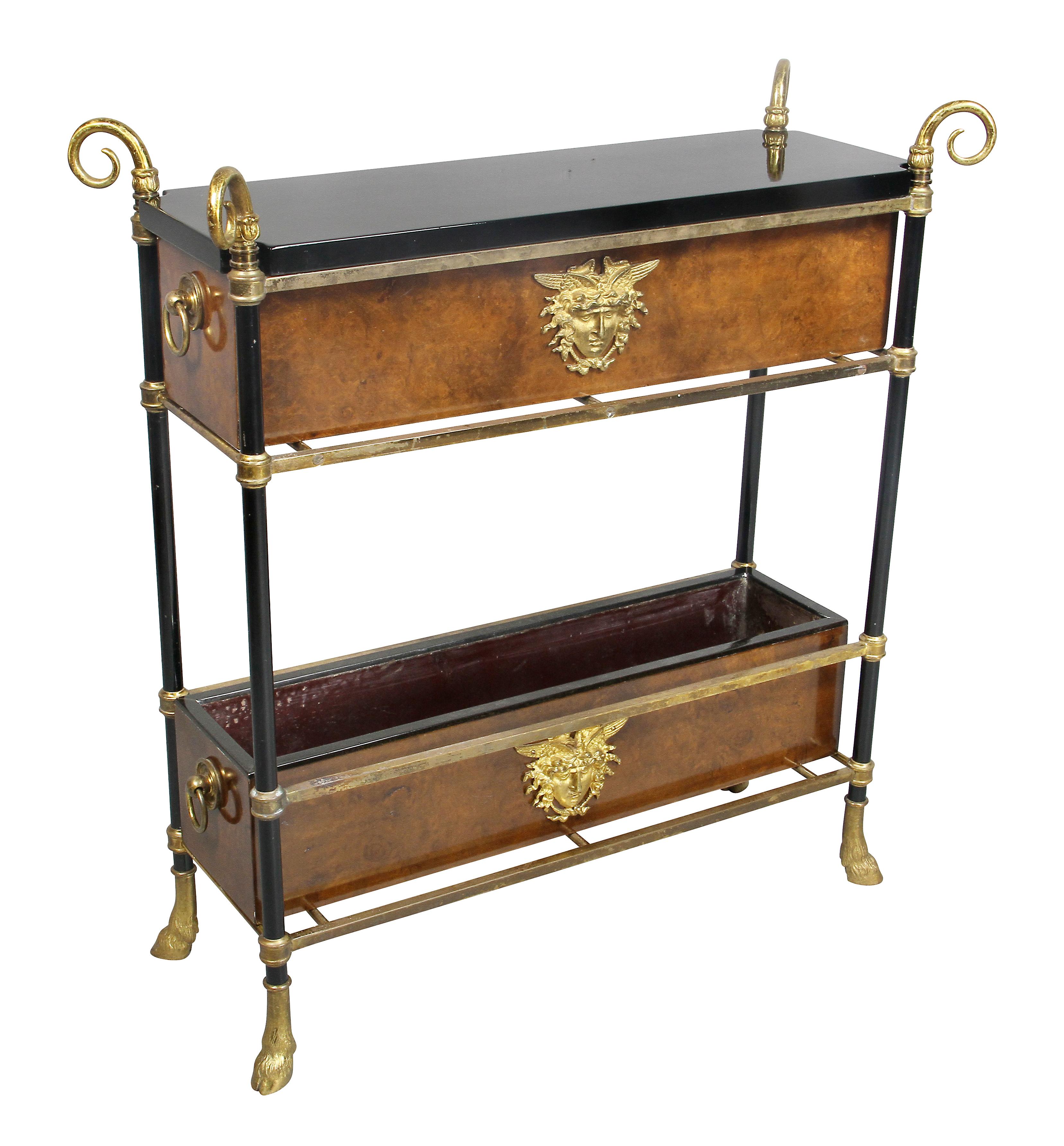 With a removable black lacquer top in a frame with scrolled brass finials opening to a compartment, the face with burl wood and applied gilt metal mask, conforming lower open tray, hoof feet.
