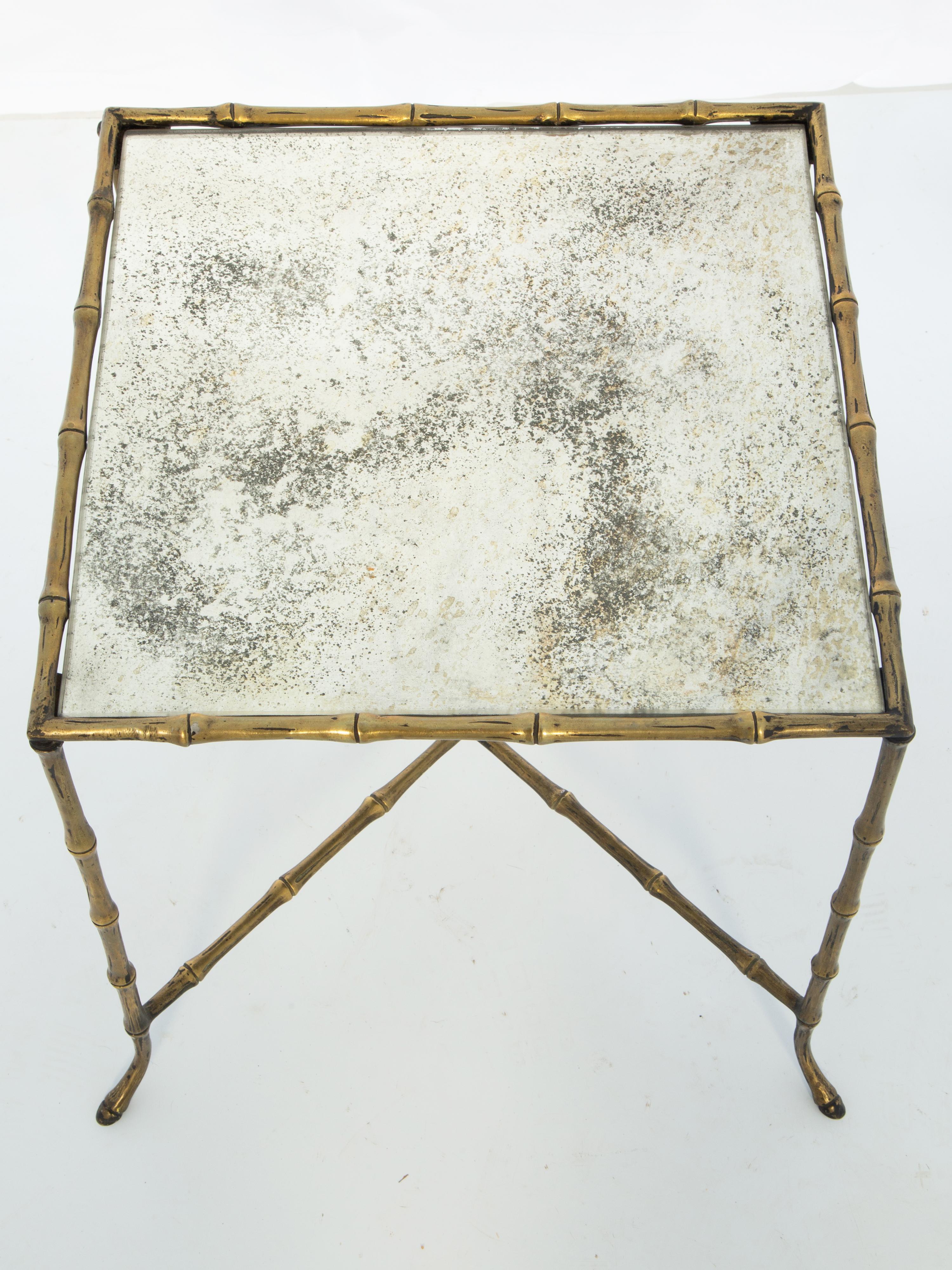 Table d'appoint vintage, en laiton, avec un plateau carré en miroir antiquaire, sa base façonnée en faux bambou, reposant sur quatre pieds, se terminant par des pieds légèrement évasés se terminant par de petits sabots.

Stock ID : D4033