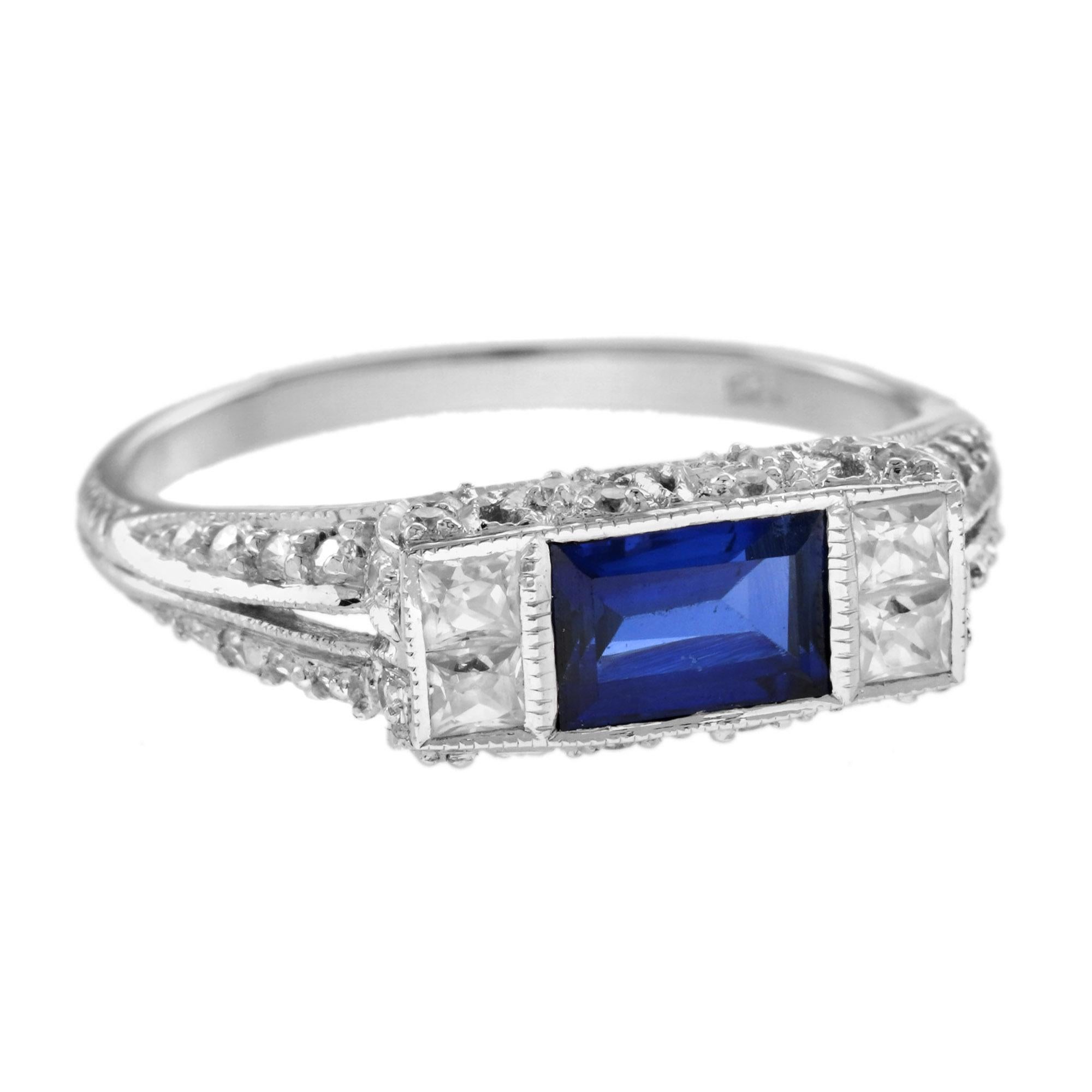 Este magnífico anillo consta de una piedra de zafiro azul en forma de baguette con cuatro diamantes cuadrados en la parte superior. La pieza está acabada con un ribete milgrain y hombros de espiga partida con diamantes, tan típico de la época, y es