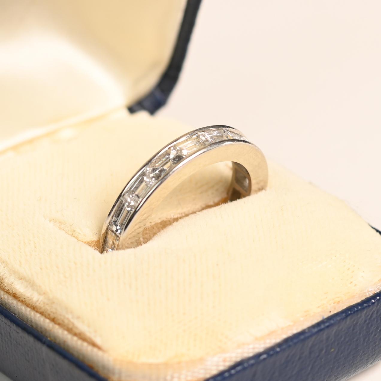 Cette exquise alliance en diamant taille baguette est un symbole intemporel de sophistication et de grâce. Dotée d'une étonnante rangée de diamants baguettes en serti-cannelé encerclant le périmètre, cette bague rayonne de brillance sous tous les