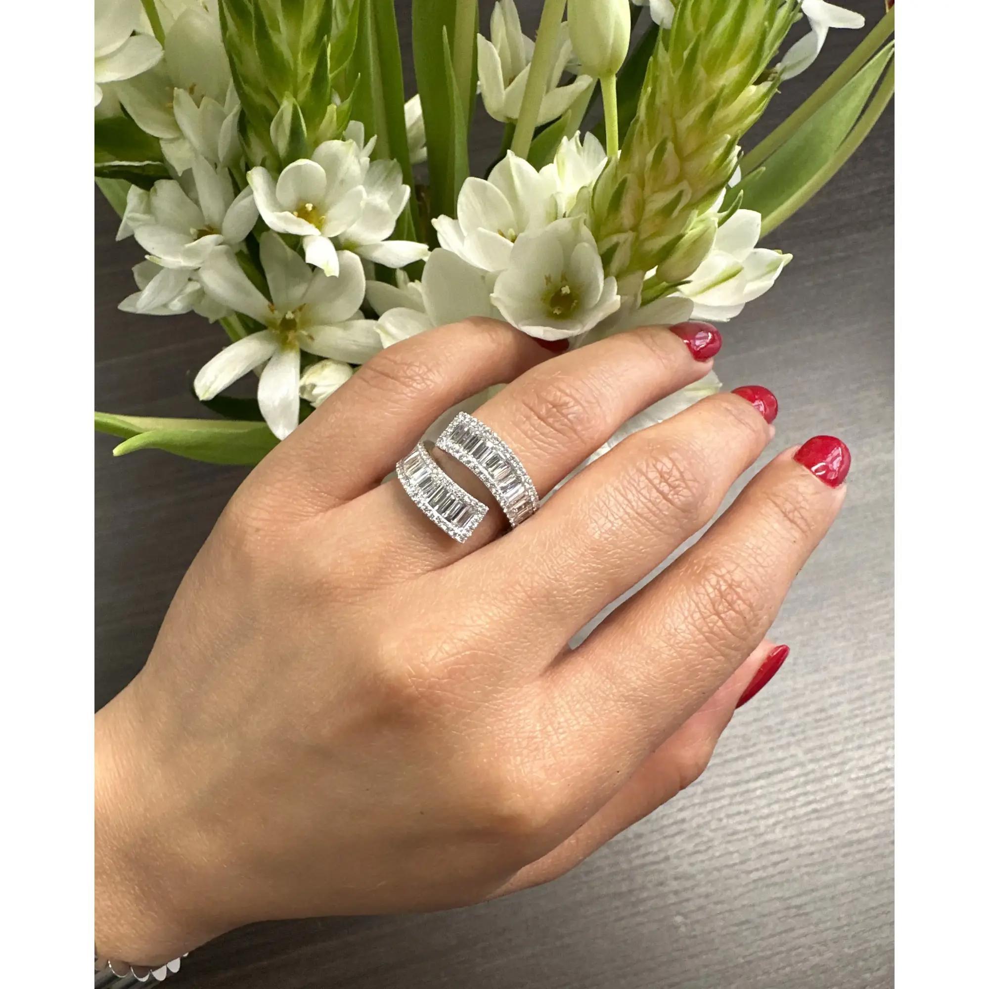 Cette magnifique bague bypass en diamant taille baguette est réalisée en or blanc 18k et met en valeur 1,90 carats de diamants taille baguette entourés de diamants taille ronde. Son design élégant allie un luxe intemporel, ce qui en fait une pièce