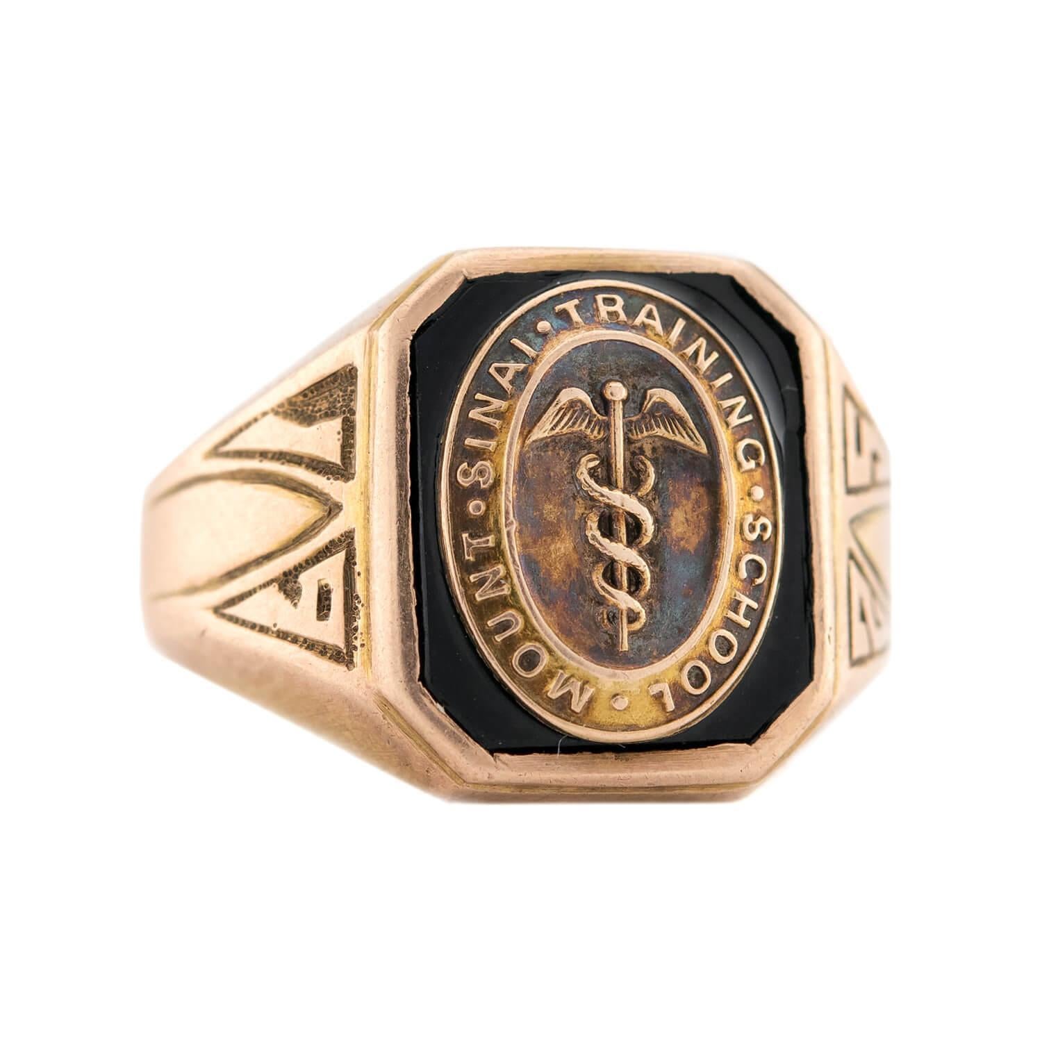 An incredible class ring by Bailey, Banks, and Biddle from the Art Deco (ca1925) era! Crafted in 14k yellow gold, this highly unique ring features a square-shaped face. The front of the face features an oval-shaped motif, which is centered by a