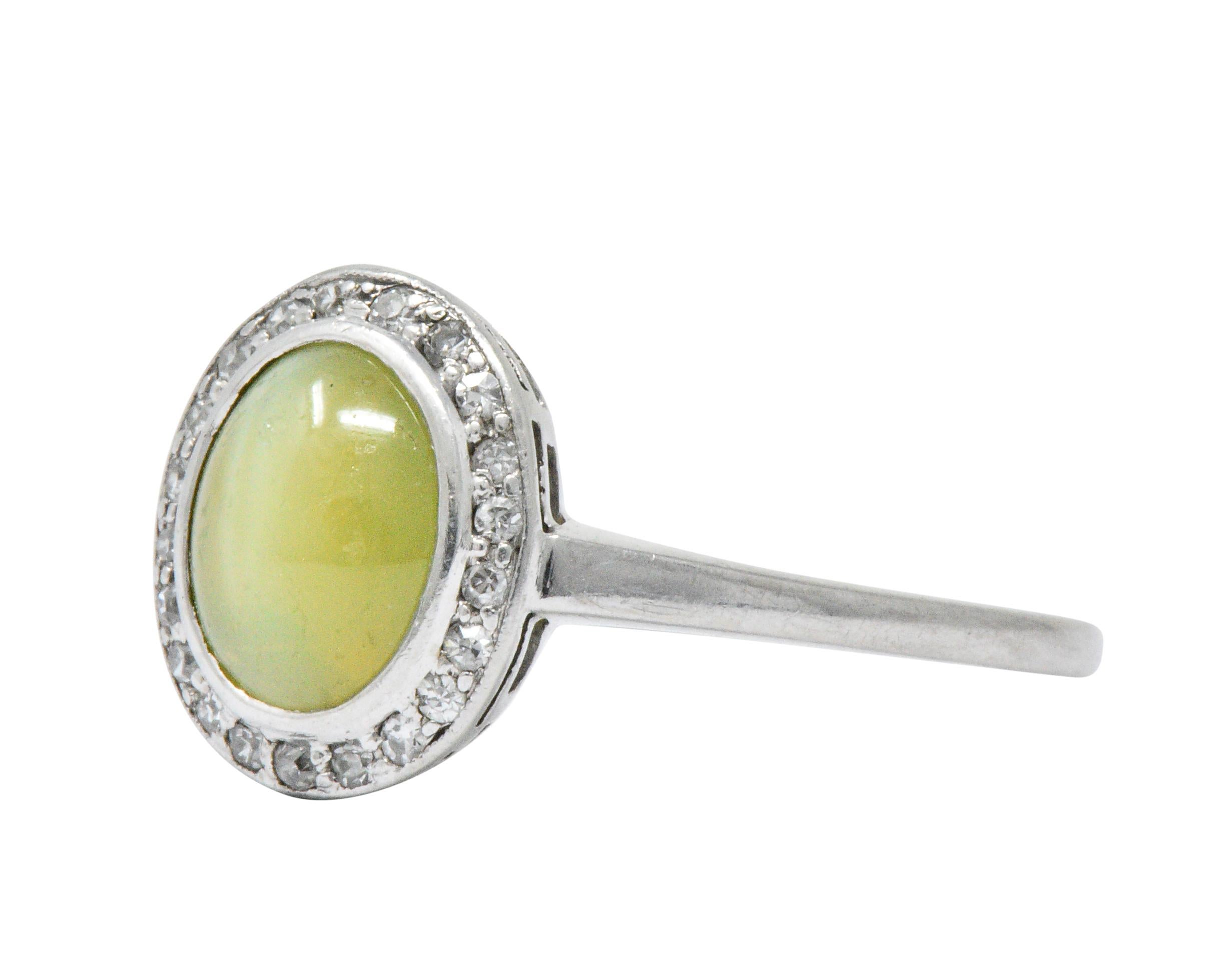 Centering a bezel set cat's eye chrysoberyl cabochon weighing approximately 2.20 carats

Translucent yellowish-green and bisected by a strongly chatoyant white line

Surrounded by a halo of single cut diamonds weighing approximately 0.10 carat