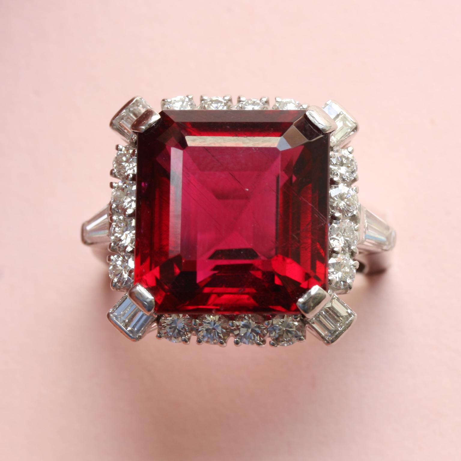 A platinum ring set with a large, bright red, step-cut rubelite (app. 12 carats), bordered with brilliant-cut diamonds and two baguette-cut diamonds in the prongs at each corner, with a tapered baguette diamond in the shank, signed: Bailey, Banks &