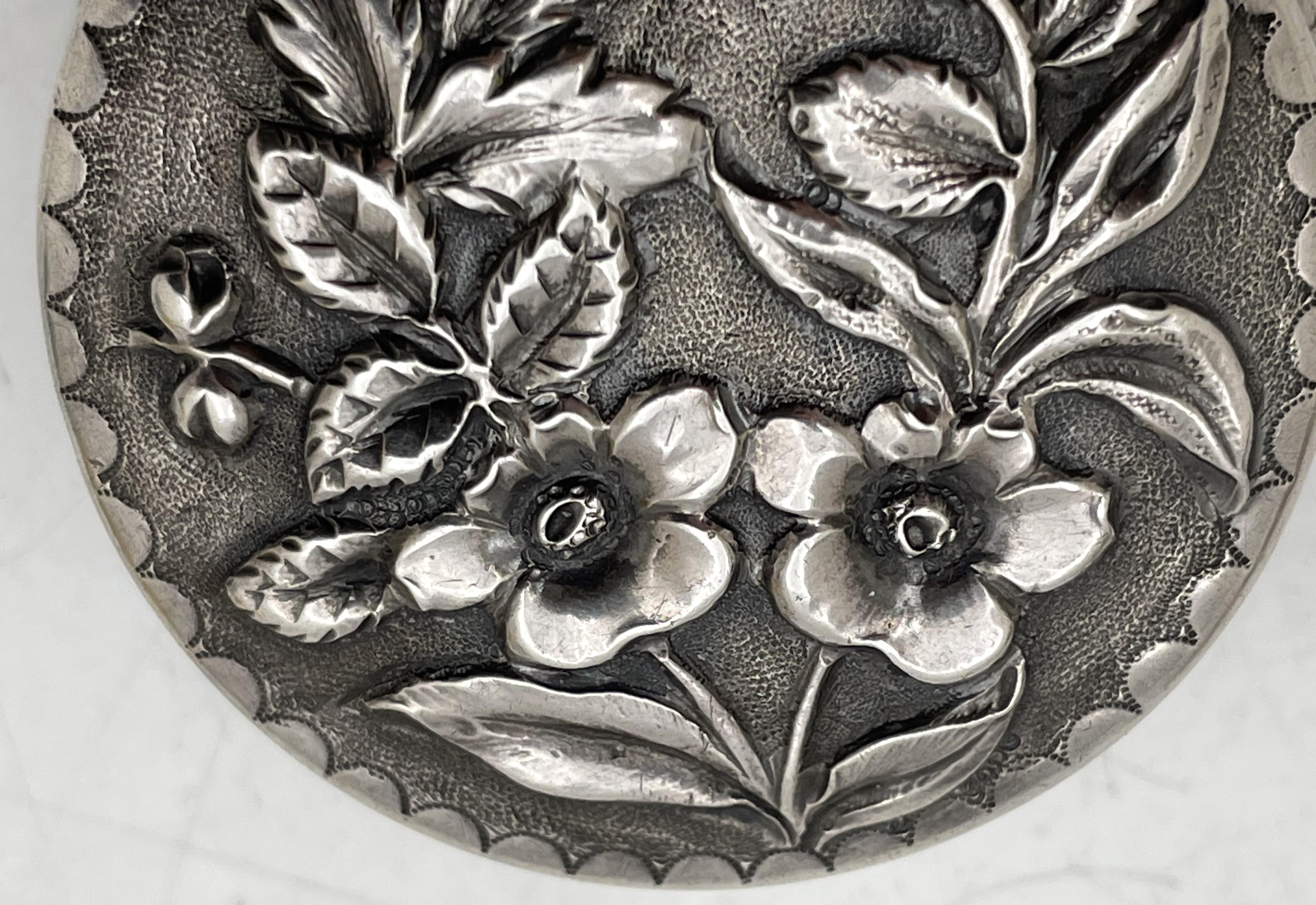 Bailey, Banks & Biddle sterling silver pill box in repousse pattern, beautifully adorned with floral motifs, gilt inside. from the late 19th century. It measures 1 7/8'' by 1/3'' in height, and bears hallmarks as shown. 

Bailey & Kitchen, as it was