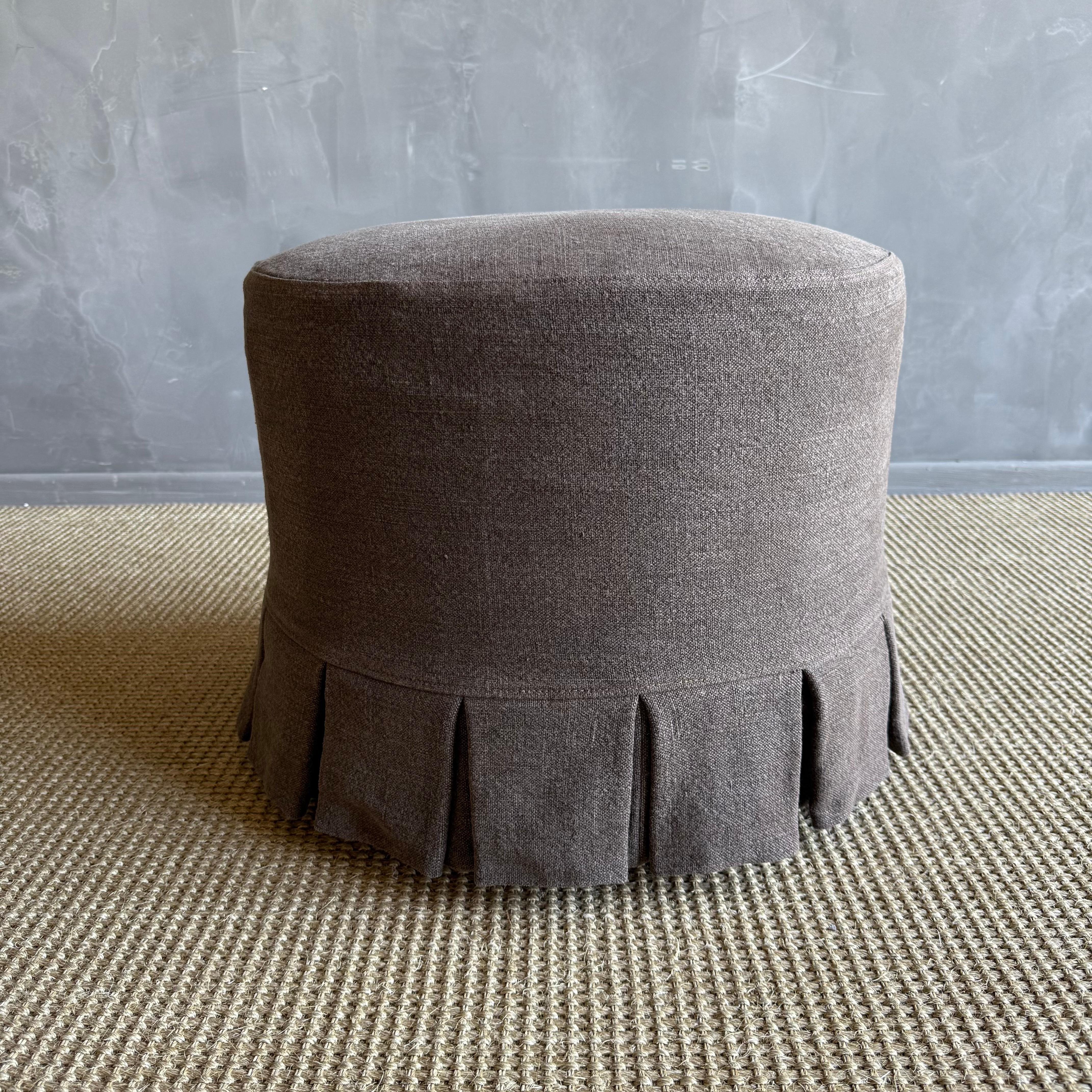 Introducing the Bailey Round Ottoman, with elegant white oak legs finished in a medium tone.

Covered in a sophisticated heavy weight hemp this ottoman is versatile and stylish, featuring a slip cover with pleated ruffle details.
The sturdy solid