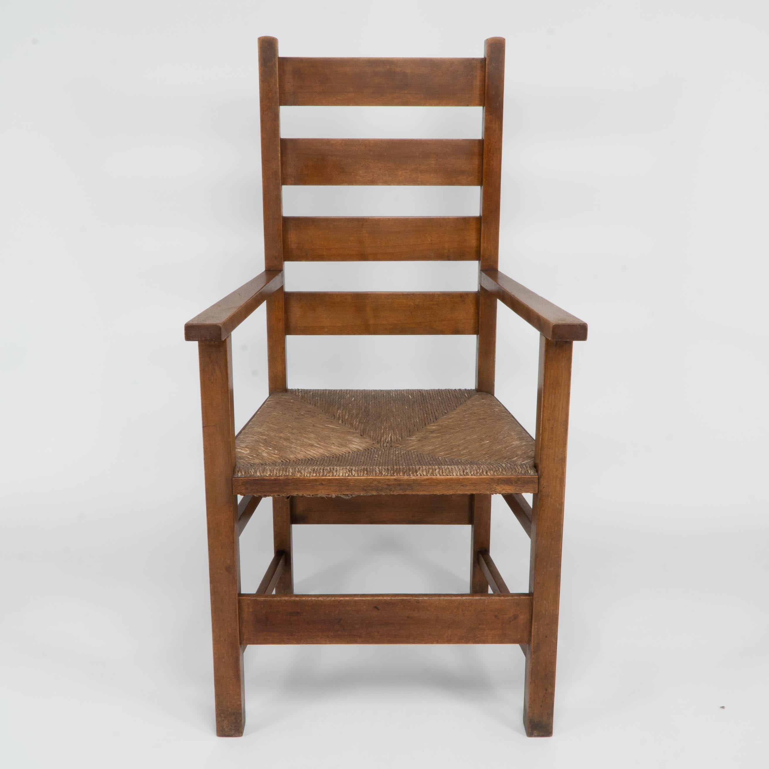 M H Baillie Scott. An Arts and Crafts oak and rush seat ladder back armchair made by J P White at The Pyghtle Works in Bedford. Illustrated in: Furniture made at The Pyghtle Works Bedford by J P White. Designed by M H Baillie Scott, Fig No 8.
