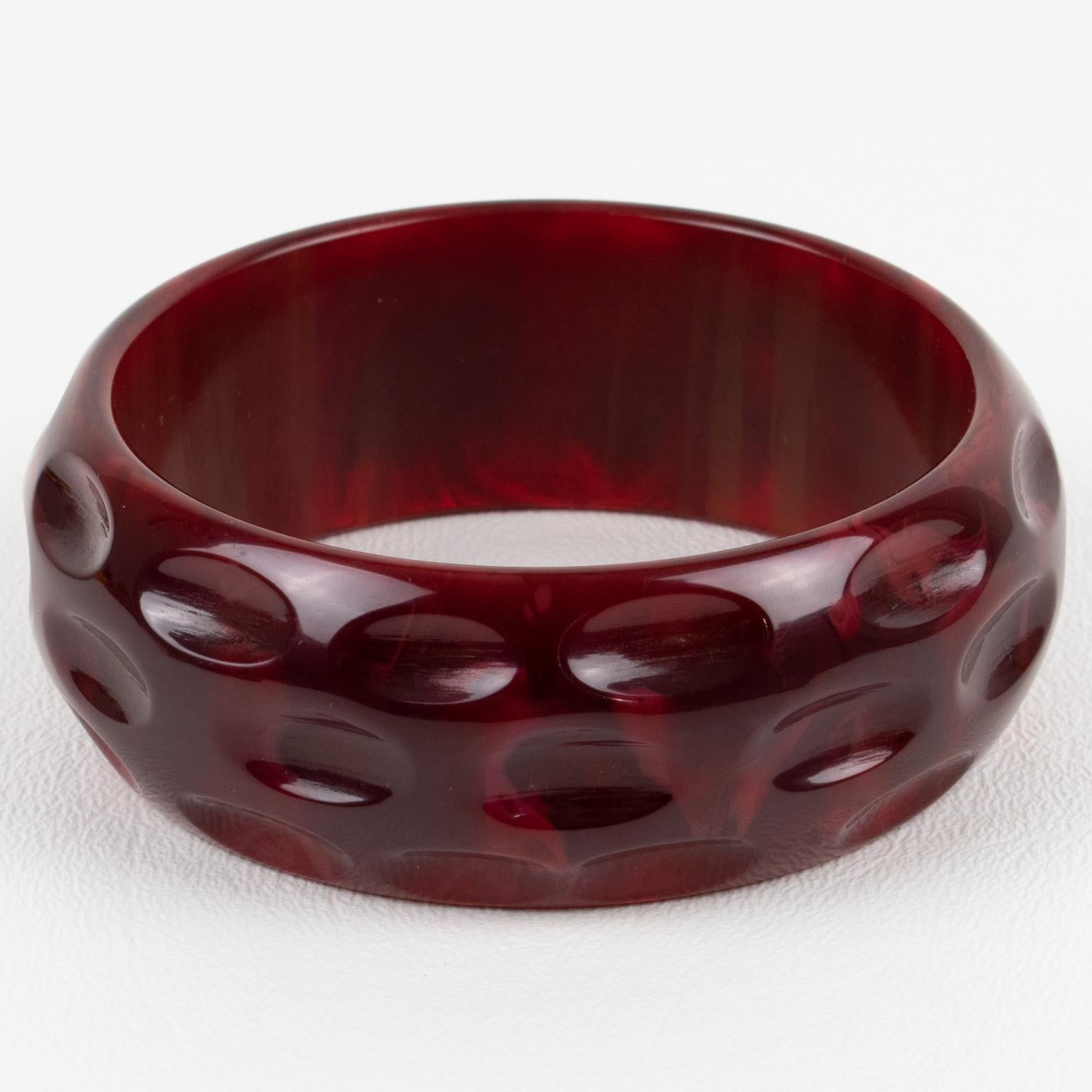 This is a stunning crimson-red marble Bakelite bracelet bangle. It features a chunky domed shape with geometric and deeply carved designs. The color is an intense red marble tone with cloudy swirling. 
Measurements: Inside across is 2.50 in diameter