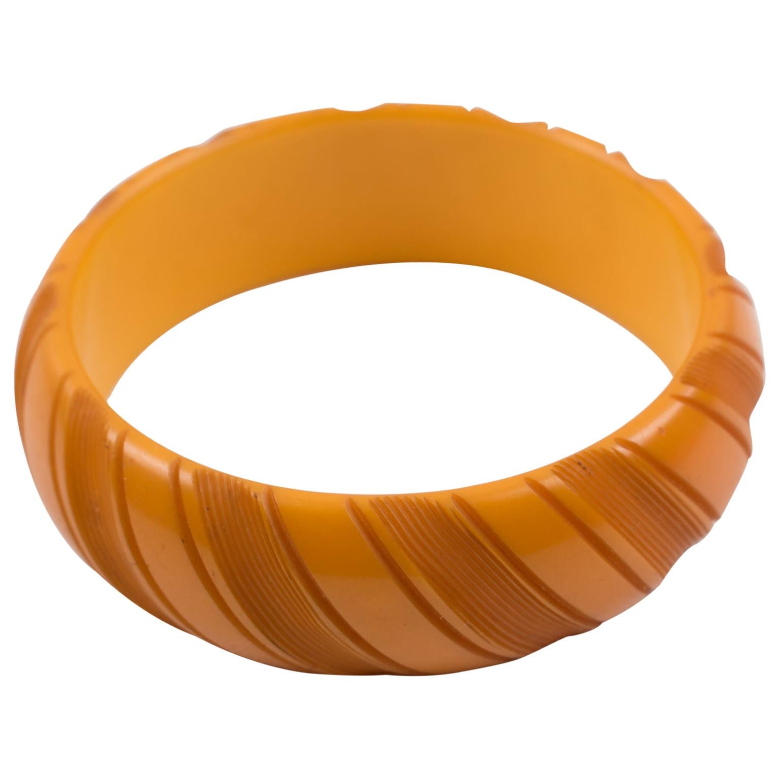 Dieser bezaubernde Bakelit-Armreif hat eine klobige, gewölbte Form mit tiefen geometrischen Schnitzereien und eine intensive, butterscotchgelbe/orange Farbe. 
Abmessungen: Innendurchmesser: 2,63 cm (6,6 cm) - Außendurchmesser: 3,19 cm (8,1 cm) -