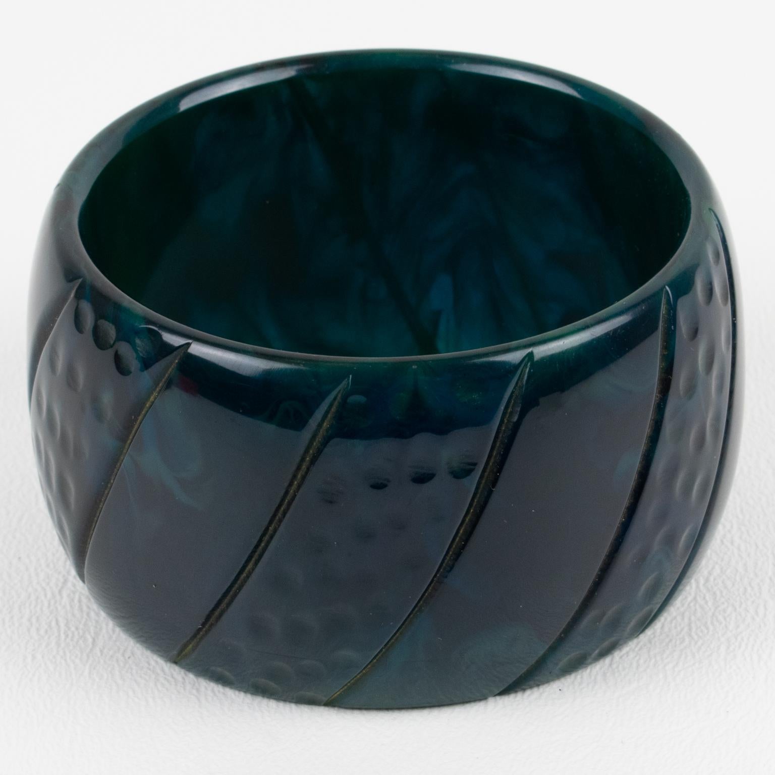 This is a superb stormy blue marble Bakelite carved bracelet bangle. It features a chunky oversized domed shape with a geometric carving design all around. The color is an intense deep navy blue tone with green and light blue swirling.