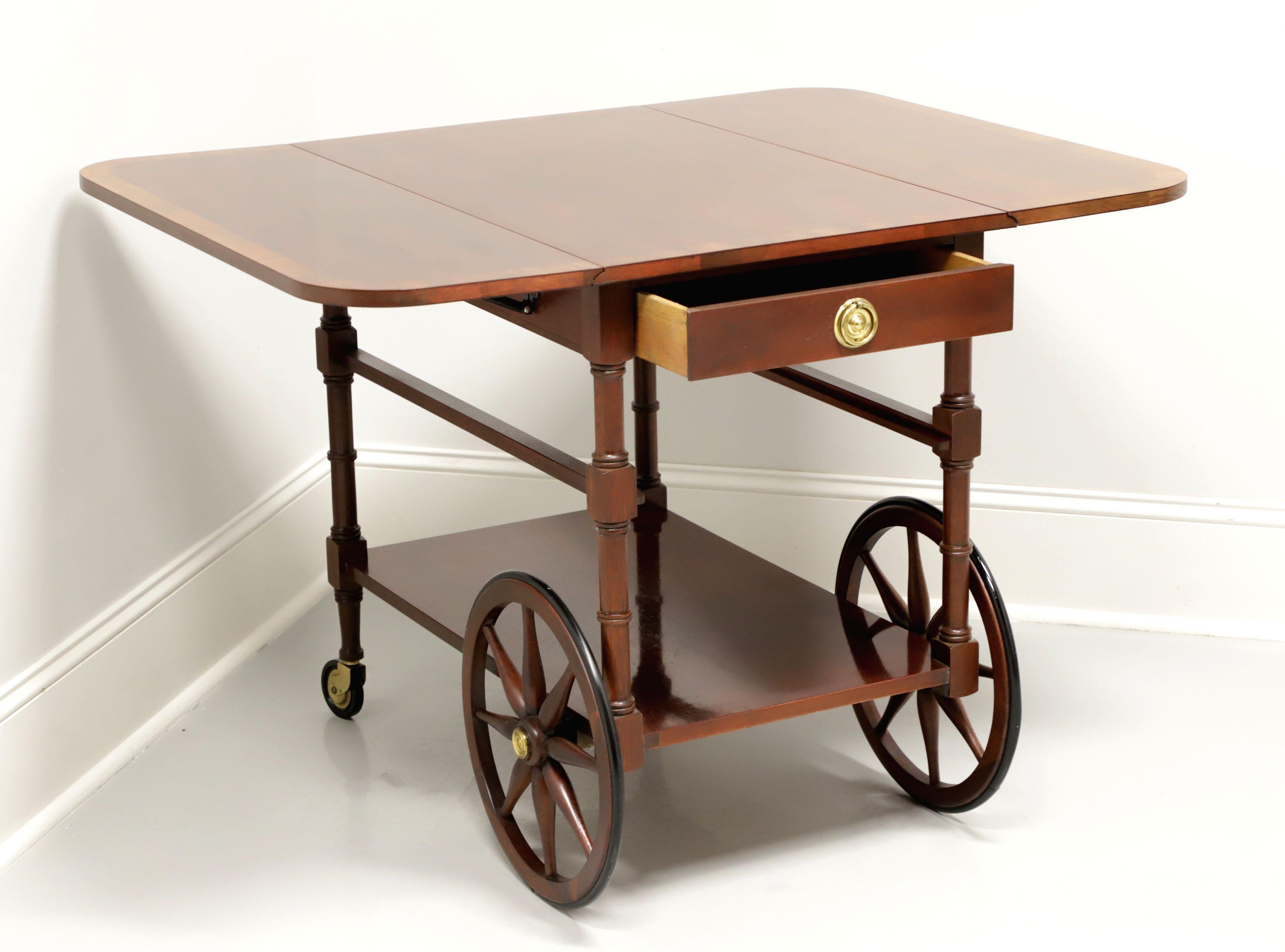 A Federal style rolling drop leaf tea cart by Baker Furniture. Mahogany with banded top, brass hardware, expandable by two drop leaves, fold-down handle, track for storing a removable tray, lower shelf, turned front legs with casters and large spoke