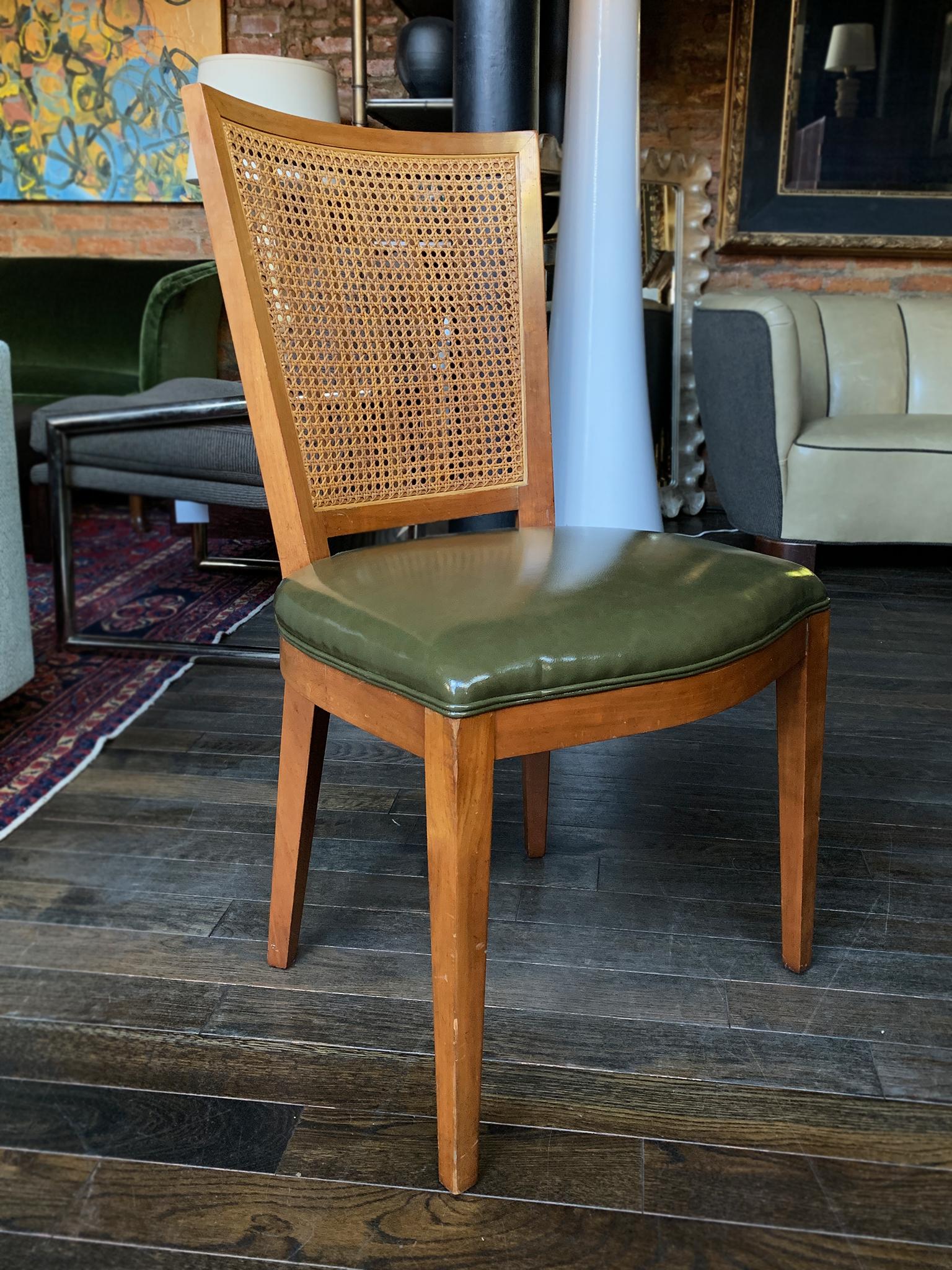 A set of 4 dining chairs made by the Baker Furniture Company in the mid-20th century. The chairs are crafted from beech wood with a caning back and new faux leather upholstery. Their height is lower than other dining chairs, and closer to the height