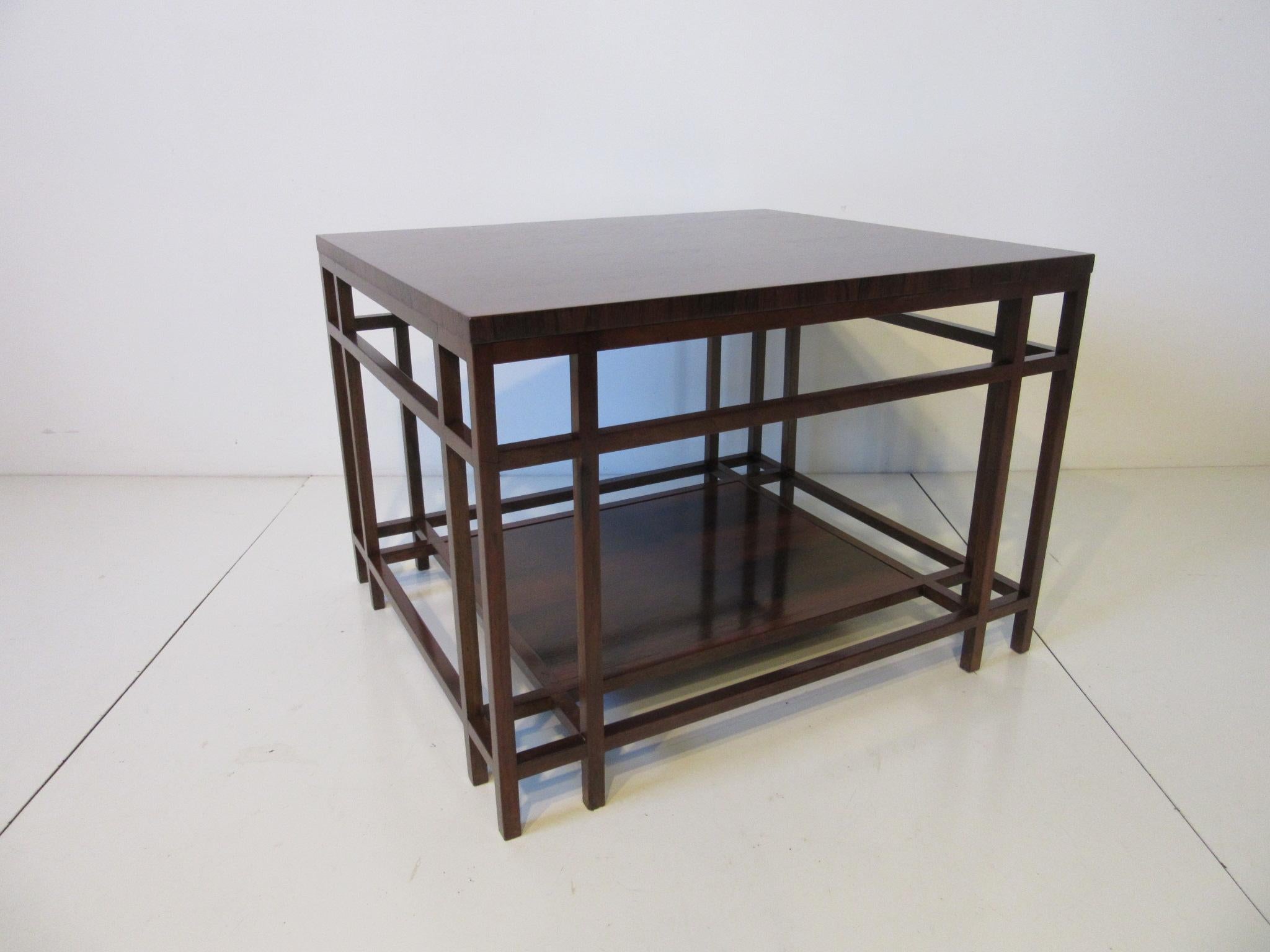 A well grained deep rich Brazilian rose wood side or end table with architectural styled base and shelve , retains the metal label manufactured by the Baker Furniture company . A well crafted piece of furniture which is typical for Baker.