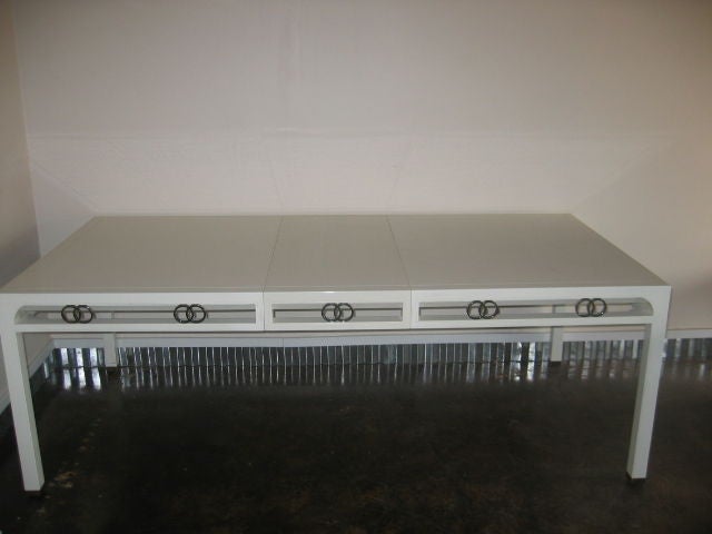 Long, white lacquered table with silver interlocking ring design on the sides. Streamline detailing. The leaf measures 18