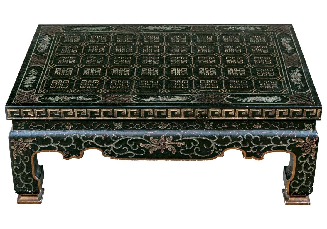 An exceptional Baker chinoiserie cocktail table lacquered black and ornately detailed with a center design of fret grids separated by diamond-shaped tiling and surrounded by a trim with maroon lattices interrupted by reserves depicting foliate