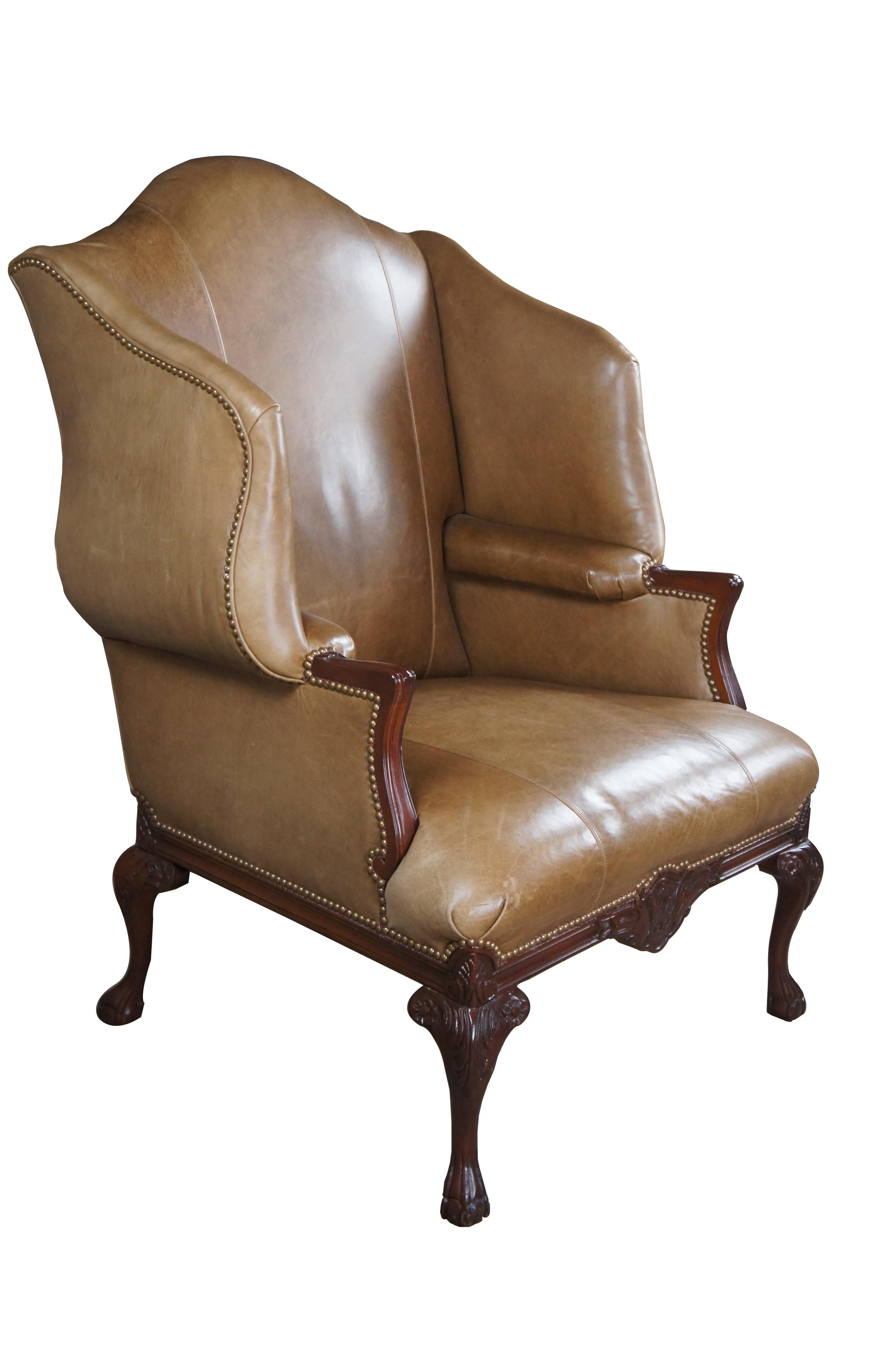Vintage Baker Furniture oversized wingback library, club or lounge chair.  Features English Chippendale styling with leather upholstery, nailhead trim and mahogany frame. The chair supported by ball and claw feet with acanthus carvings at the